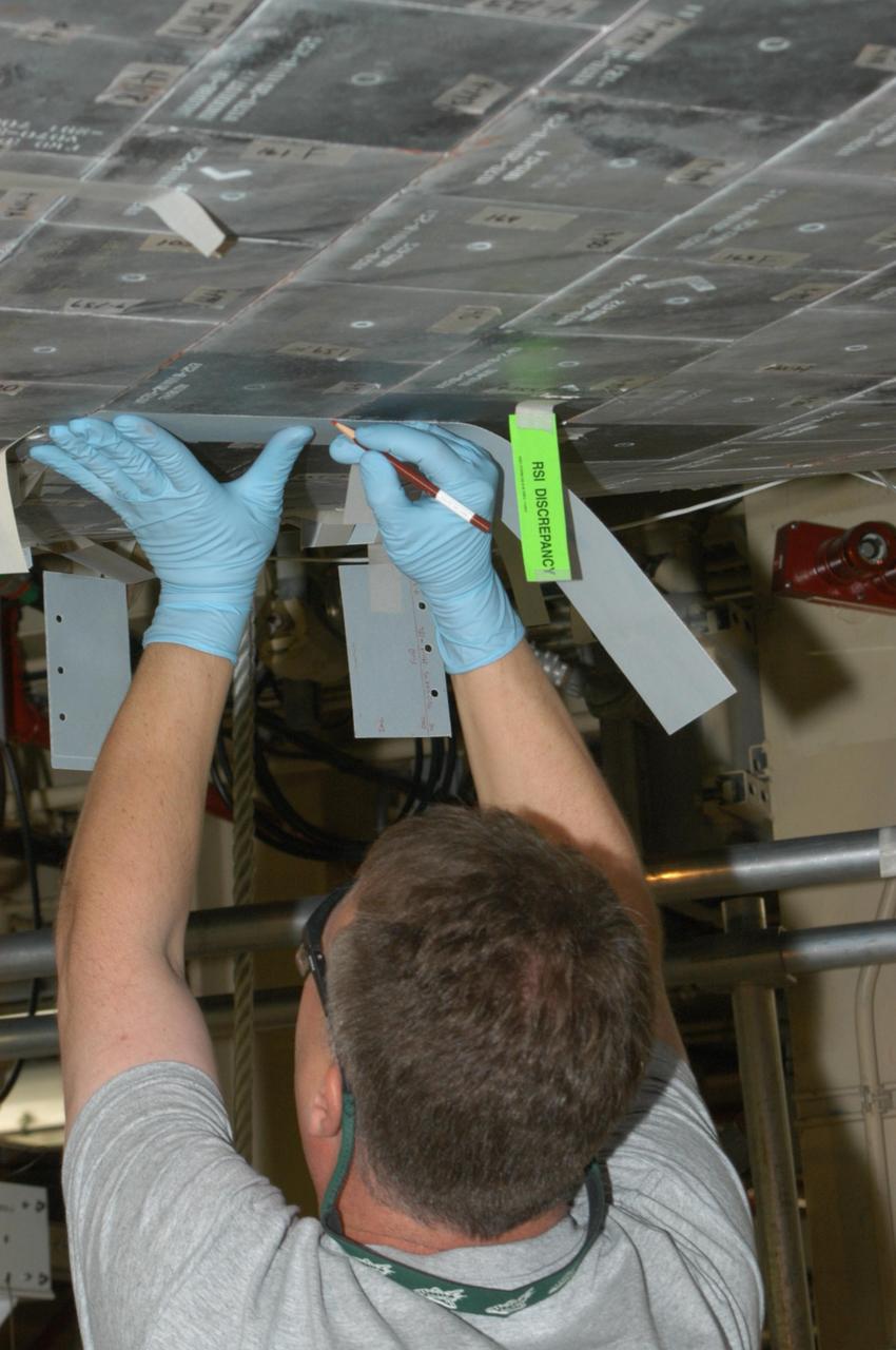 KENNEDY SPACE CENTER, FLA. --  United Space Alliance technician Larry Tanner places a strip of gap filler on the tile of Discovery’s underbelly to measure it for installation. Discovery is being processed in Orbiter Processing Facility Bay 3 at NASA’s Kennedy Space Center.  This work is being performed due to two gap fillers that were protruding from the underside of Discovery on the first Return to Flight mission, STS-114. New installation procedures have been developed to ensure the gap fillers stay in place and do not pose any hazard during the shuttle's re-entry to the atmosphere. Discovery is the scheduled orbiter for the second space shuttle mission in the return-to-flight sequence.