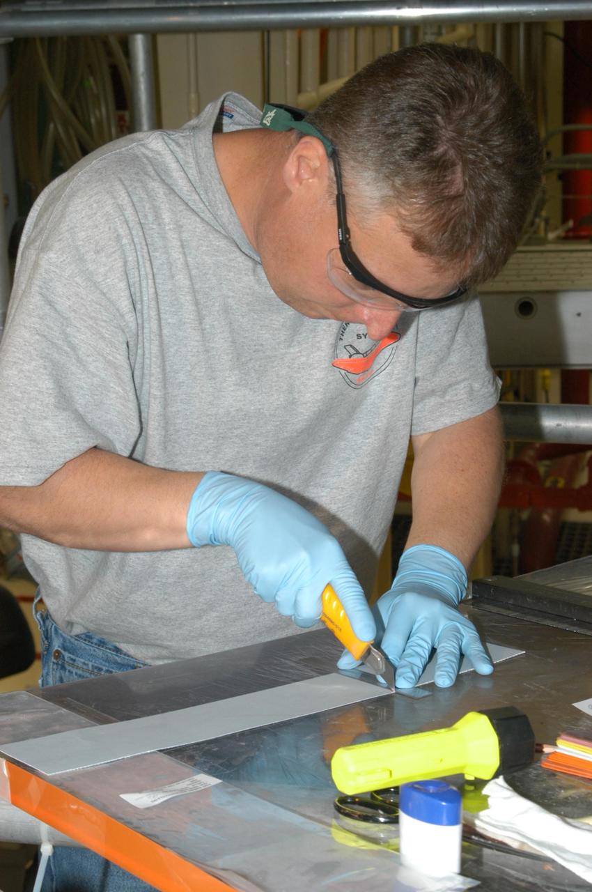 KENNEDY SPACE CENTER, FLA. --  United Space Alliance technician Larry Tanner cuts the strip of gap filler to be installed on the orbiter Discovery, which is being processed in Orbiter Processing Facility Bay 3 at NASA’s Kennedy Space Center.  This work is being performed due to two gap fillers that were protruding from the underside of Discovery on the first Return to Flight mission, STS-114. New installation procedures have been developed to ensure the gap fillers stay in place and do not pose any hazard during the shuttle's re-entry to the atmosphere. Discovery is the scheduled orbiter for the second space shuttle mission in the return-to-flight sequence.