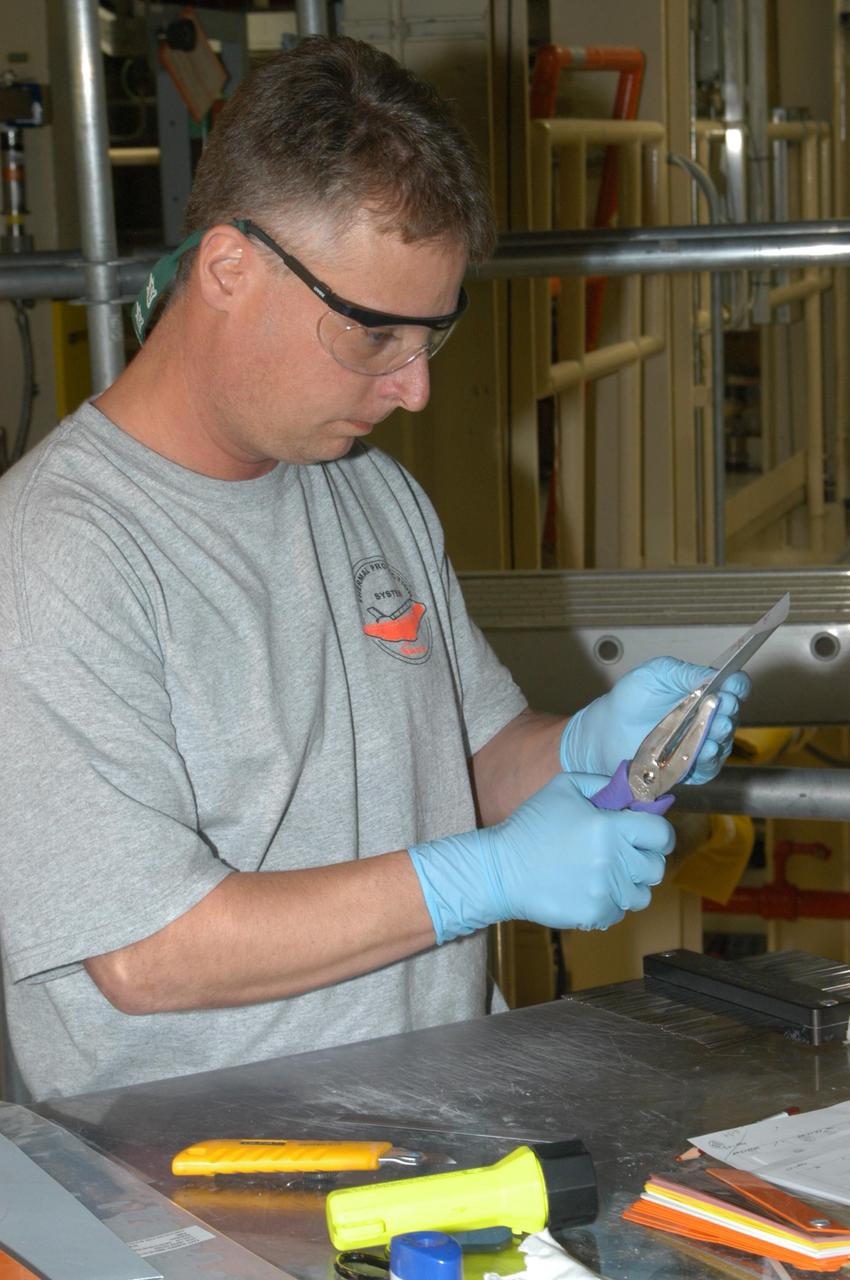 KENNEDY SPACE CENTER, FLA. --  United Space Alliance technician Larry Tanner punches three holes in the gap filler to be installed on Discovery.  The holes are used for the string pull test done after installation to ensure the gap filler is bonded  properly. Discovery is being processed in Orbiter Processing Facility Bay 3 at NASA’s Kennedy Space Center.  This work is being performed due to two gap fillers that were protruding from the underside of Discovery on the first Return to Flight mission, STS-114. New installation procedures have been developed to ensure the gap fillers stay in place and do not pose any hazard during the shuttle's re-entry to the atmosphere. Discovery is the scheduled orbiter for the second space shuttle mission in the return-to-flight sequence.