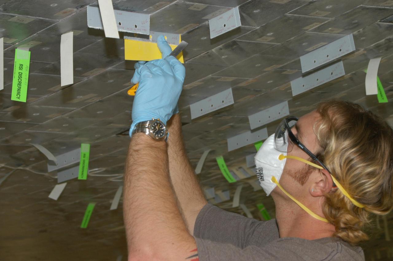 KENNEDY SPACE CENTER, FLA. -- United Space Alliance technician Shane Colvin prepares to cut the excess gap filler from the tile on the orbiter Discovery, which is being processed in Orbiter Processing Facility Bay 3 at NASA’s Kennedy Space Center.  This work is being performed due to two gap fillers that were protruding from the underside of Discovery on the first Return to Flight mission, STS-114. New installation procedures have been developed to ensure the gap fillers stay in place and do not pose any hazard during the shuttle's re-entry to the atmosphere. Discovery is the scheduled orbiter for the second space shuttle mission in the return-to-flight sequence.