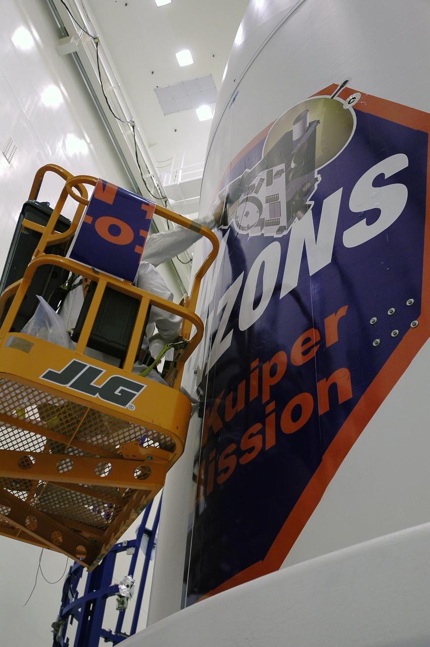KENNEDY SPACE CENTER, FLA. - Technicians install strips of the New Horizons mission decal on the spacecraft fairing in the Payload Hazardous Servicing Facility. The last strip will be installed on the fairing after the spacecraft is delivered to Pad 41 on Dec. 17. New Horizons carries seven scientific instruments that will characterize the global geology and geomorphology of Pluto and its moon Charon, map their surface compositions and temperatures, and examine Pluto's complex atmosphere. After that, flybys of Kuiper Belt objects from even farther in the solar system may be undertaken in an extended mission. New Horizons is the first mission in NASA's New Frontiers program of medium-class planetary missions. The spacecraft, designed for NASA by the Johns Hopkins University Applied Physics Laboratory in Laurel, Md., will launch aboard a Lockheed Martin Atlas V rocket and fly by Pluto and Charon as early as summer 2015.