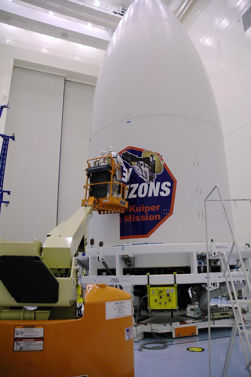KENNEDY SPACE CENTER, FLA. - Technicians install strips of the New Horizons mission decal on the spacecraft fairing in the Payload Hazardous Servicing Facility. The last strip will be installed on the fairing after the spacecraft is delivered to Pad 41 on Dec. 17. New Horizons carries seven scientific instruments that will characterize the global geology and geomorphology of Pluto and its moon Charon, map their surface compositions and temperatures, and examine Pluto's complex atmosphere. After that, flybys of Kuiper Belt objects from even farther in the solar system may be undertaken in an extended mission. New Horizons is the first mission in NASA's New Frontiers program of medium-class planetary missions. The spacecraft, designed for NASA by the Johns Hopkins University Applied Physics Laboratory in Laurel, Md., will launch aboard a Lockheed Martin Atlas V rocket and fly by Pluto and Charon as early as summer 2015.