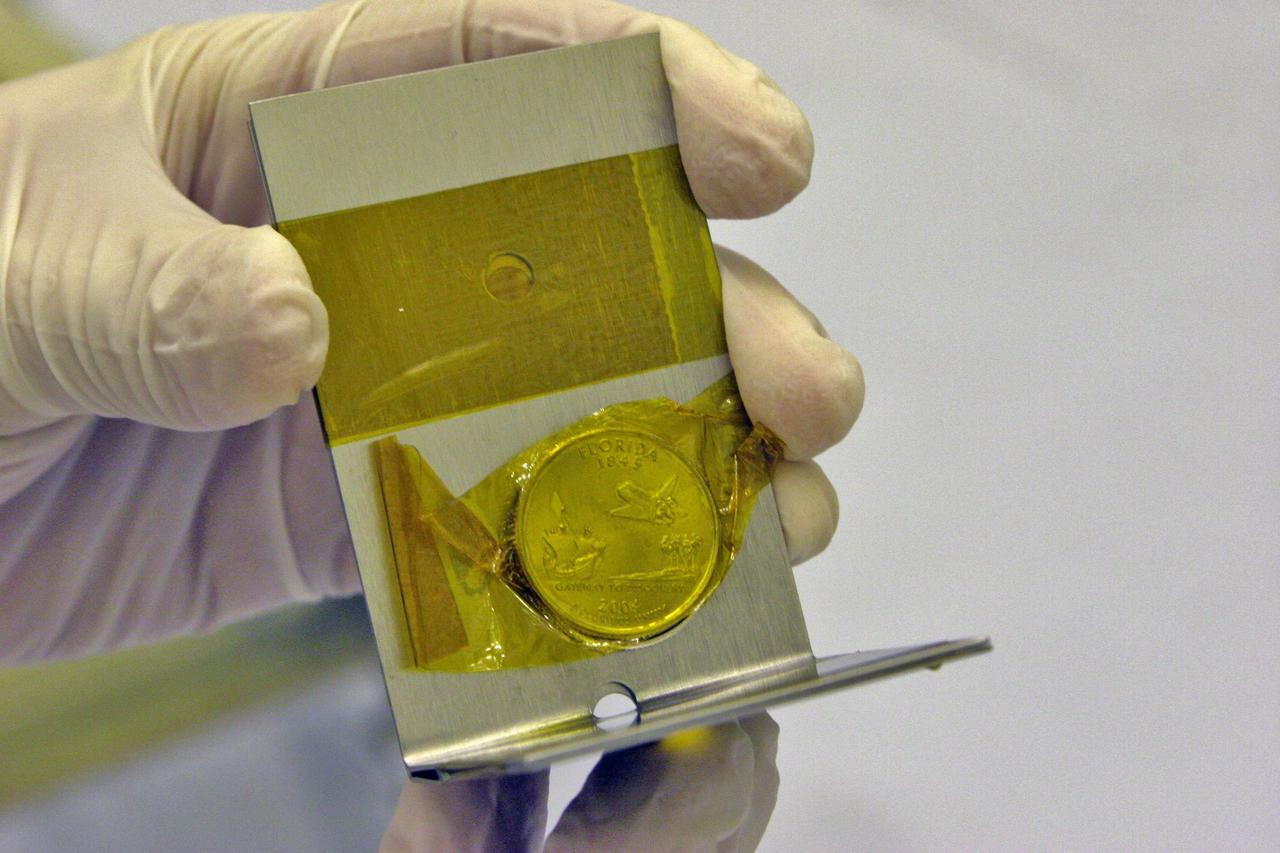 KENNEDY SPACE CENTER, FLA. - A Florida quarter is prepared for installation on the New Horizons spacecraft in Kennedy Space Center's Payload Hazardous Servicing Facility. The new quarter, engraved with the "Gateway to Discovery" design, will accompany New Horizons on its 3-billion-mile journey to the planet Pluto and its moon, Charon. Although appropriate for the mission to carry the coin from the state that symbolizes space exploration, it will also serve a practical purpose: scientists are using the quarter as a spin-balance weight. New Horizons comprises seven scientific instruments that will characterize the global geology and geomorphology of Pluto and its moon Charon, map their surface compositions and temperatures, and examine Pluto's complex atmosphere. After that, flybys of Kuiper Belt objects from even farther in the solar system may be undertaken in an extended mission. New Horizons is the first mission in NASA's New Frontiers program of medium-class planetary missions. The spacecraft, designed for NASA by the Johns Hopkins University Applied Physics Laboratory in Laurel, Md., will launch aboard a Lockheed Martin Atlas V rocket and fly by Pluto and Charon as early as summer 2015. Photo Credit: Applied Physics Laboratory/George W. Rogers III