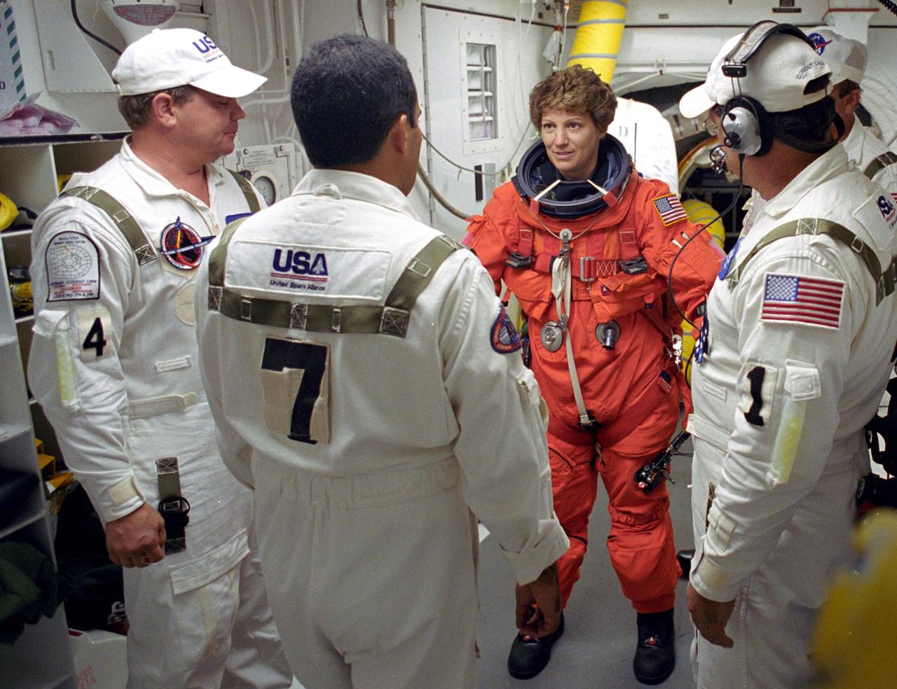 KENNEDY SPACE CENTER, FLA. - STS-114 Mission Commander Eileen Collins is helped by the Closeout Crew with her launch and entry suit before entering Space Shuttle Discovery. The Return to Flight mission to the International Space Station carries the External Stowage Platform-2, equipped with spare part assemblies, and a replacement Control Moment Gyroscope contained in the Lightweight Multi-Purpose Experiment Support Structure and Multi-Purpose Logistics Module Raffaello, housing 15 tons of hardware and supplies that will be transferred to the Station after the Shuttle docks to the complex . On this mission, the crew will perform inspections on-orbit for the first time of all of the Reinforced Carbon-Carbon (RCC) panels on the leading edge of the wings and the Thermal Protection System tiles using the new Canadian-built Orbiter Boom Sensor System and the data from 176 impact and temperature sensors. Mission Specialists will also practice repair techniques on RCC and tile samples during a spacewalk in the payload bay.