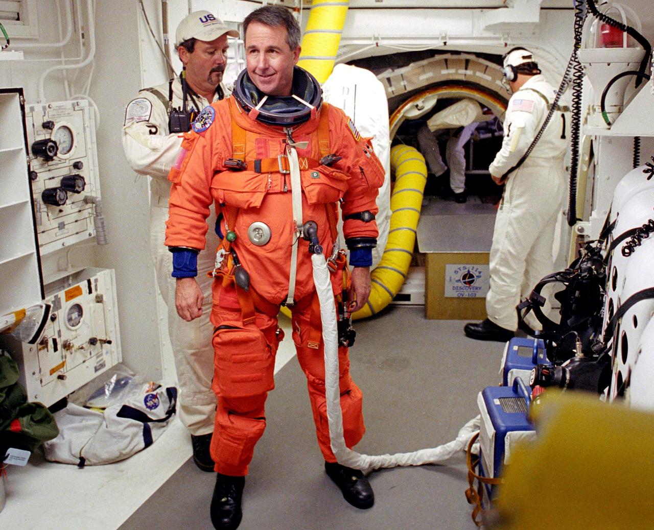 KENNEDY SPACE CENTER, FLA. - STS-114 Mission Specialist Stephen Robinson is helped by the Closeout Crew with his launch and entry suit before entering Space Shuttle Discovery. The Return to Flight mission to the International Space Station carries the External Stowage Platform-2, equipped with spare part assemblies, and a replacement Control Moment Gyroscope contained in the Lightweight Multi-Purpose Experiment Support Structure and Multi-Purpose Logistics Module Raffaello, housing 15 tons of hardware and supplies that will be transferred to the Station after the Shuttle docks to the complex . On this mission, the crew will perform inspections on-orbit for the first time of all of the Reinforced Carbon-Carbon (RCC) panels on the leading edge of the wings and the Thermal Protection System tiles using the new Canadian-built Orbiter Boom Sensor System and the data from 176 impact and temperature sensors. Mission Specialists will also practice repair techniques on RCC and tile samples during a spacewalk in the payload bay.