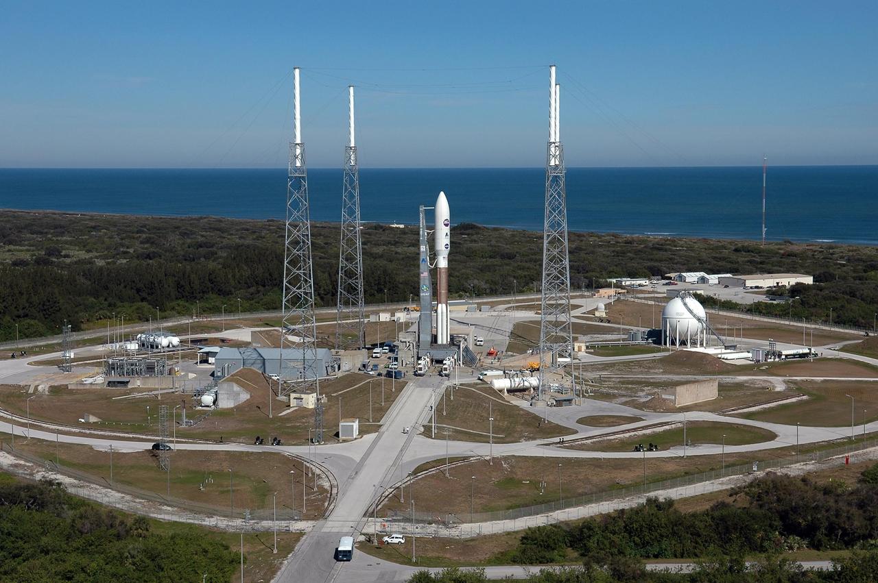 KENNEDY SPACE CENTER, FLA. -  With the backdrop of blue sky and blue water of the Atlantic Ocean, the Atlas V expendable launch vehicle with the New Horizons spacecraft (center) is nearly ready for launch.  Surrounding the rocket are lightning masts that support the catenary wire used to provide lightning protection.  The liftoff is scheduled for 1:24 p.m. EST Jan. 17.  After its launch aboard the Atlas V, the compact, 1,050-pound piano-sized probe will get a boost from a kick-stage solid propellant motor for its journey to Pluto. New Horizons will be the fastest spacecraft ever launched, reaching lunar orbit distance in just nine hours and passing Jupiter 13 months later. The New Horizons science payload, developed under direction of Southwest Research Institute, includes imaging infrared and ultraviolet spectrometers, a multi-color camera, a long-range telescopic camera, two particle spectrometers, a space-dust detector and a radio science experiment. The dust counter was designed and built by students at the University of Colorado, Boulder. A launch before Feb. 3 allows New Horizons to fly past Jupiter in early 2007 and use the planet’s gravity as a slingshot toward Pluto. The Jupiter flyby trims the trip to Pluto by as many as five years and provides opportunities to test the spacecraft’s instruments and flyby capabilities on the Jupiter system. New Horizons could reach the Pluto system as early as mid-2015, conducting a five-month-long study possible only from the close-up vantage of a spacecraft.