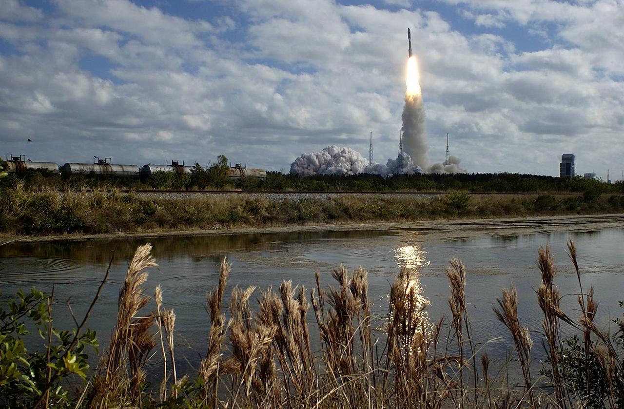 KENNEDY SPACE CENTER, FLA. — The fiery launch of NASA’s New Horizons spacecraft aboard a Lockheed Martin Atlas V rocket is reflected in the nearby creek. Liftoff was on time at 2 p.m. EST from Complex 41 on Cape Canaveral Air Force Station in Florida. Railroad cars (center left) are stopped on the tracks that run near the complex. Photo credit: NIKON/Scott Andrews