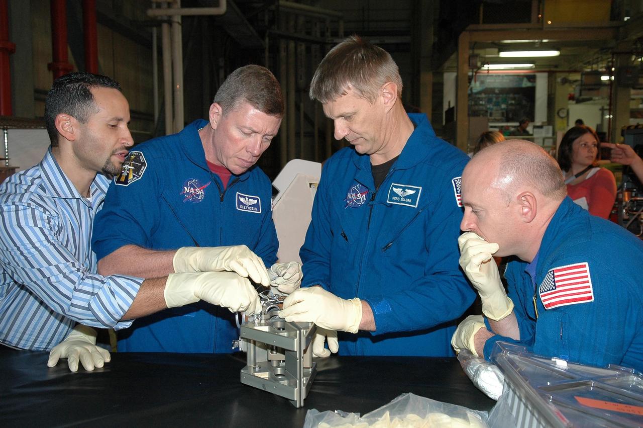KENNEDY SPACE CENTER, FLA. - In NASA Kennedy Space Center's Orbiter Processing Facility bay 3, members of the STS-121 crew, under the watchful eyes of Tomas Gonzalez-Torres, with NASA's Johnson Space Center, practice working with hardware for the mission. Seen are (second from left) Mission Specialists Michael Fossum and Piers Sellers and Pilot Mark Kelly. The crew is at Kennedy to take part in the crew equipment interface test, which provides hands-on experience with equipment to be used on-orbit. Launch of Space Shuttle Discovery on mission STS-121, the second return-to-flight mission, is scheduled no earlier than May.