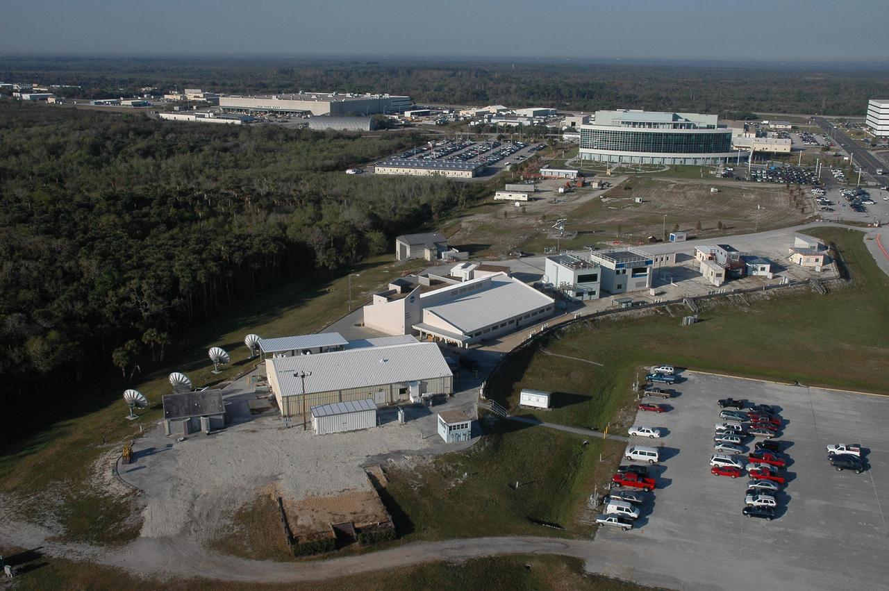 KENNEDY SPACE CENTER, FLA. - This aerial view shows the Press Site (in the foreground) comprising the NASA TV studio, the NASA News Center behind it, buildings used by local NBC and CBS television stations, and newly erected prefabricated buildings for local newspapers and correspondents for CNN, AP and others. A year-long project removed and replaced hurricane-hazardous trailers and bleachers from the site. In the background, at right, is the newly build Operations Support Building II. Photo credit: Cory Huston