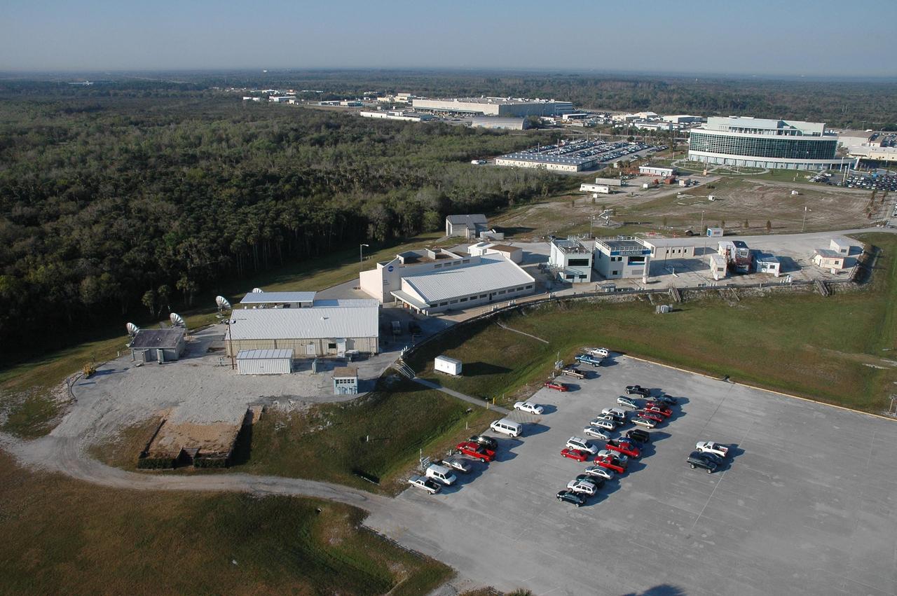 KENNEDY SPACE CENTER, FLA. - This aerial view shows the Press Site (in the foreground) comprising the NASA TV studio, the NASA News Center behind it, buildings used by local NBC and CBS television stations, and newly erected prefabricated buildings for local newspapers and correspondents for CNN, AP and others. A year-long project removed and replaced hurricane-damaged trailers and grandstands from the site. In the background, at right, is the newly built Operations Support Building II, which replaced modular housing and trailers in the Launch Complex 39 area. Photo credit: Cory Huston