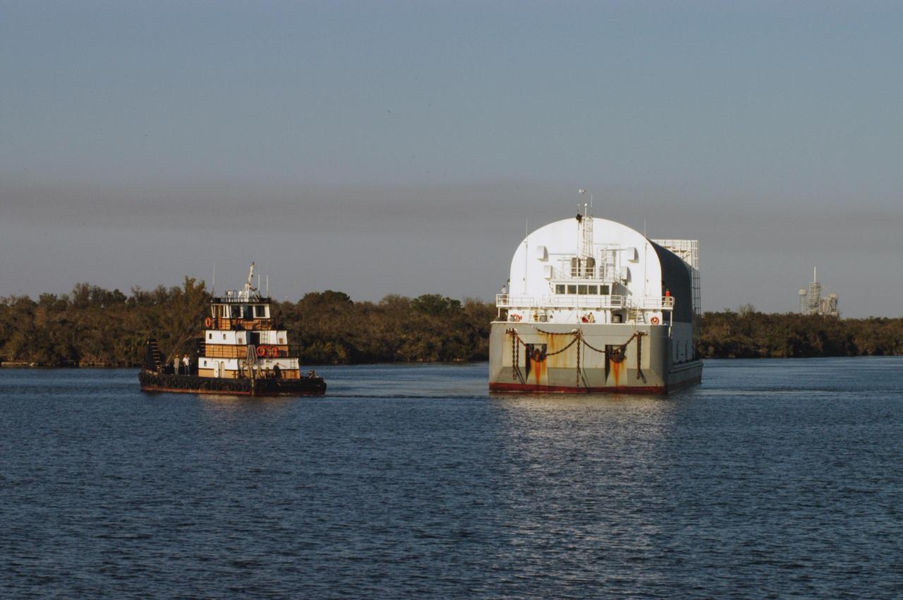 KENNEDY SPACE CENTER, FLA.  - One of the two space shuttle launch pads in Launch Complex 39 is visible behind the Pegasus barge as it traverses the turn basin near the Vehicle Assembly Building. The barge is on the last leg of its journey from the Michoud Assembly Facility in New Orleans to NASA's Kennedy Space Center.  The barge carries the redesigned external fuel tank that will launch Space Shuttle Discovery on the next shuttle mission, STS-121.  After off-loading, the tank will be moved into the Vehicle Assembly Building and lifted into a checkout cell for further work. The tank, designated ET-119, will fly with many major safety changes, including the removal of the protuberance air load ramps. A large piece of foam from a ramp came off during the last shuttle launch in July 2005. The ramps were removed to eliminate a potential source of damaging debris to the space shuttle.  The next launch of Discovery is scheduled for May 2006.