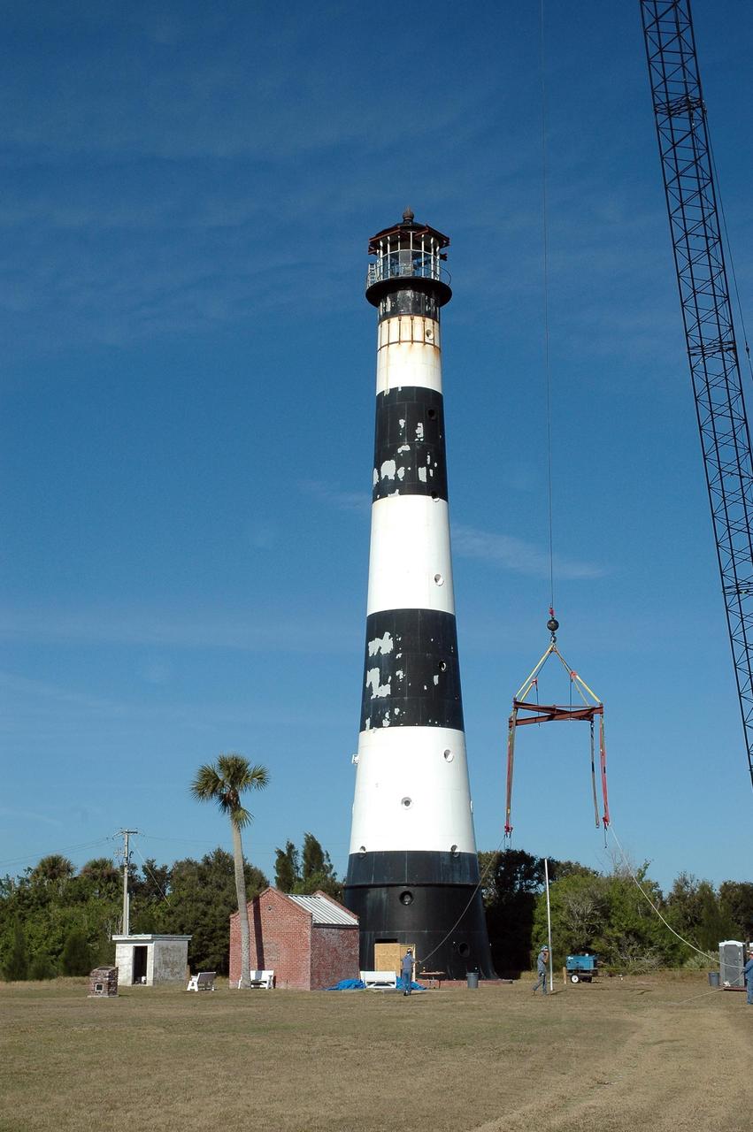 KENNEDY SPACE CENTER, FLA.  - At Cape Canaveral Air Force Station, a crane is lifted near the Cape Canaveral Lighthouse for use in removing the lamp room at top. Leaks in the roof allowed moisture to seep in. The lamp room is being removed for repairs and refurbishment.  In addition, the original brass roof will be restored and put back in place. The Cape Canaveral Lighthouse is the only operational lighthouse owned by the Air Force. It was first erected in 1868 near the edge of the Atlantic Ocean.  Photo credit: NASA/Jack Pfaller