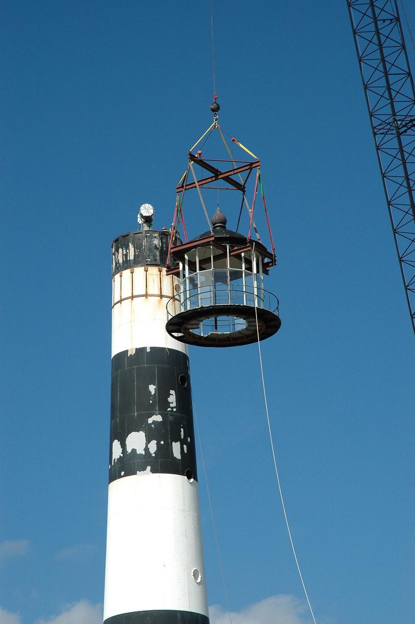 KENNEDY SPACE CENTER, FLA.  - At Cape Canaveral Air Force Station,  a crane lowers the detached lamp room alongside the Cape Canaveral Lighthouse. Leaks in the roof allowed moisture to seep in.  The lamp room is being removed for repairs and refurbishment.  In addition, the original brass roof will be restored and put back in place. The Cape Canaveral Lighthouse is the only operational lighthouse owned by the Air Force. It was first erected in 1868 near the edge of the Atlantic Ocean.  Photo credit: NASA/Jack Pfaller