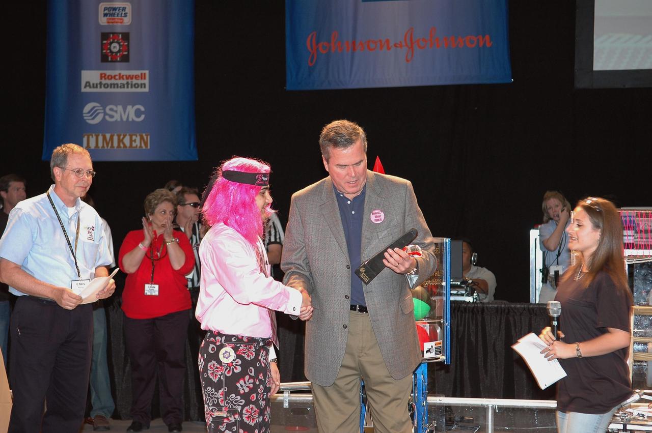 KENNEDY SPACE CENTER, FLA.  - During opening ceremonies of the  2006 FIRST Robotics Regional Competition held March 9-11 at the University of Central Florida in Orlando, Florida Governor Jeb Bush receives the inaugural Governor's Award trophy from Sam Mallikarjunan from Rockledge High School and Stephanie Alphonso from Freedom High School in Orlando.  The FIRST  Robotics Competition challenges teams of young people and their mentors to solve a common problem in a six-week timeframe using a standard "kit of parts" and a common set of rules. Teams build robots from the parts and enter them in a series of competitions.  FIRST, which is based on "For Inspiration and Recognition of Science and Technology," redefines winning for these students. Teams are rewarded for excellence in design, demonstrated team spirit, gracious professionalism and maturity, and ability to overcome obstacles. Scoring the most points is a secondary goal. Winning means building partnerships that last.  NASA and the University of Central Florida are co-sponsors of the regional event, which this year included more than 50 teams.  Photo credit: NASA/Kim Shiflett