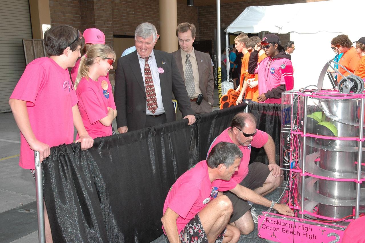 KENNEDY SPACE CENTER, FLA.  -  During the 2006 FIRST Robotics Regional Competition held March 9-11 at the University of Central Florida in Orlando, Kennedy Space Center Director Jim Kennedy and his intern Neil Berger talk with students on the Cocoa Beach High School-Rockledge High School robotic team known as the "Pink Team," which was co-sponsored by NASA KSC.  The team's robot, at right, is called Roccobot.  At least four teams in the competition were sponsored by KSC, NASA and contractors.   The FIRST  Robotics Competition challenges teams of young people and their mentors to solve a common problem in a six-week timeframe using a standard "kit of parts" and a common set of rules. Teams build robots from the parts and enter them in a series of competitions.  FIRST, which is based on "For Inspiration and Recognition of Science and Technology," redefines winning for these students. Teams are rewarded for excellence in design, demonstrated team spirit, gracious professionalism and maturity, and ability to overcome obstacles. Scoring the most points is a secondary goal. Winning means building partnerships that last.  NASA and the University of Central Florida are co-sponsors of the regional event, which this year included more than 50 teams.  Photo credit: NASA/Kim Shiflett