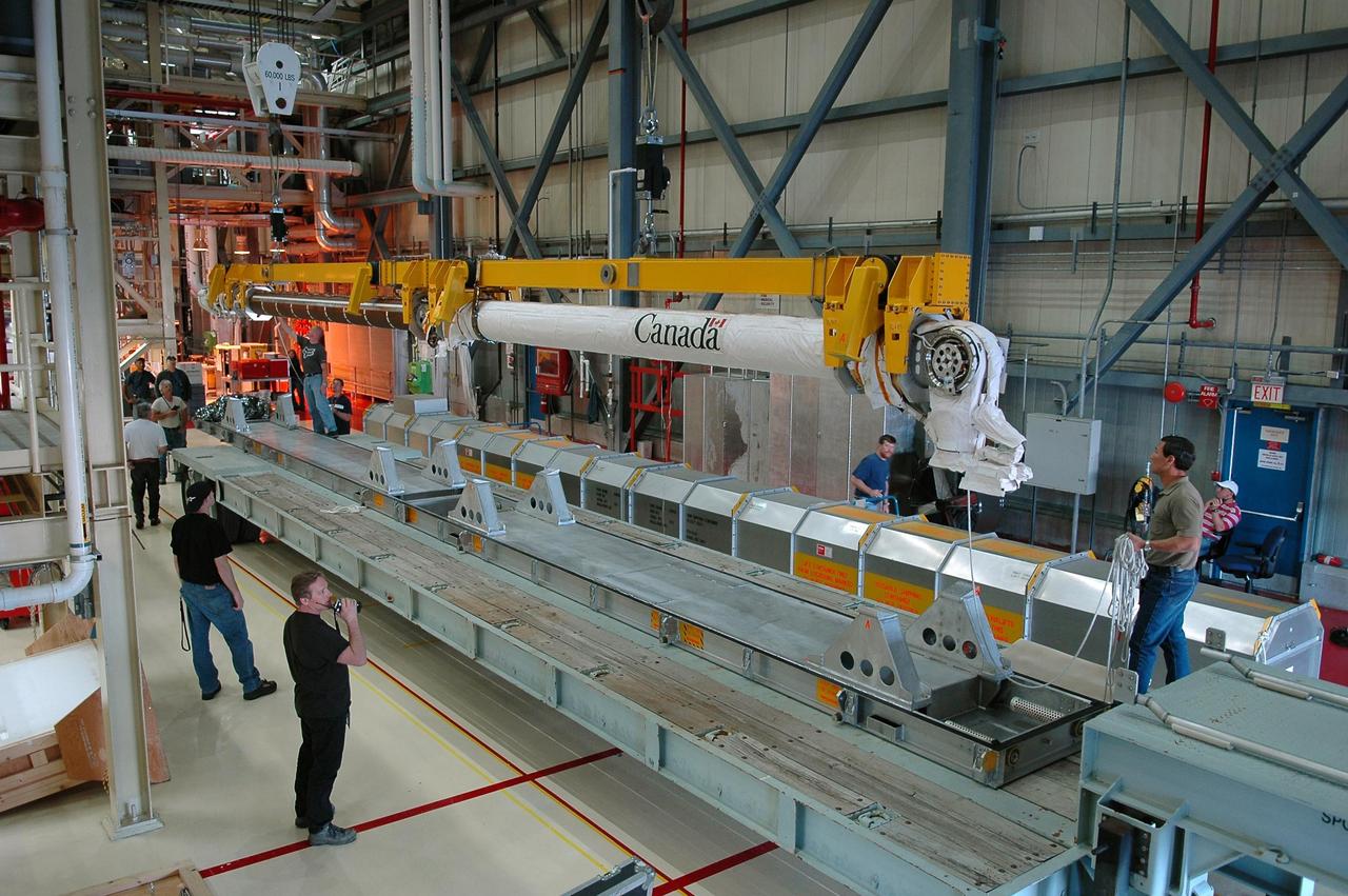 KENNEDY SPACE CENTER, FLA. - Inside the Orbiter Processing Facility bay 3 at NASA's Kennedy Space Center, workers lower Discovery's robotic arm onto a flat bed in a work area. The arm was removed from Discovery's payload bay. The arm was removed due to damage found on the arm after it was accidentally bumped by a bridge bucket in the payload bay. Ultrasound inspections revealed a small crack, measuring 1.25 inches by 0.015 inch deep. The arm will be sent back to the vendor for repair. The bucket was being used by technicians cleaning the area and was in the process of being stowed. A bridge bucket is a personnel transport device that is suspended from an overhead bridge that moves back and forth above the shuttle's mid-body. It allows workers to access the payload bay area without walking or standing on the payload bay floor or on the fixed platforms. Space Shuttle Discovery is scheduled for launch on mission STS-121 during a launch planning window of July 1-19. Photo credit: NASA/Kim Shiflett