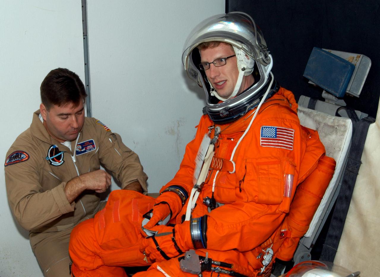KENNEDY SPACE CENTER, FLA.  -    Inside the orbiter mockup at NASA Kennedy Space Center's Shuttle Landing Facility, volunteer "astronaut" Charlie Plain, with InDyne Inc., gets settled in a seat with the help of United Space Alliance Insertion Tech Mike Thompson before a simulated emergency landing of a shuttle crew.  Known as a Mode VI exercise, the operation uses volunteer workers from the Center to pose as astronauts. The purpose of the simulation is to exercise emergency preparedness personnel, equipment and facilities in rescuing astronauts from a downed orbiter and providing immediate medical attention. Photo credit: NASA/George Shelton