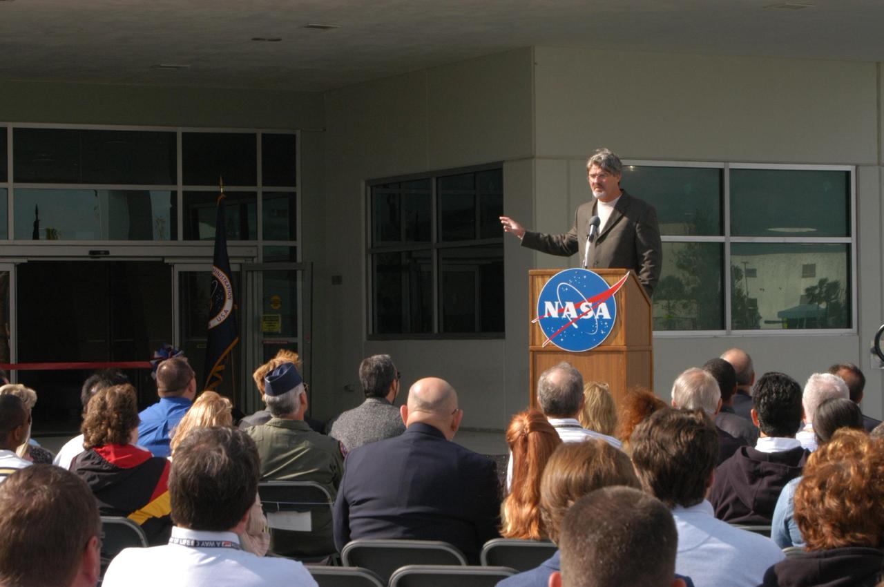 KENNEDY SPACE CENTER, FLA. --  Kennedy Space Center Deputy Director Bill Parsons explains the significance of the Operations Support Building II (behind him) to guests at the ribbon-cutting ceremony. The Operations Support Building II is an Agency safety and health initiative project to replace 198,466 square feet of substandard modular housing and trailers in the Launch Complex 39 area at Kennedy Space Center.  The five-story building, which sits south of the Vehicle Assembly Building and faces the launch pads,  includes 960 office spaces, 16 training rooms, computer and multimedia conference rooms, a Mission Conference Center with an observation deck, technical libraries, an Exchange store, storage, break areas, and parking. Photo credit: NASA/George Shelton
