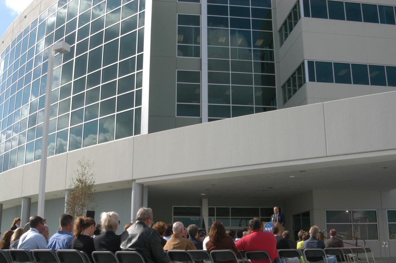 KENNEDY SPACE CENTER, FLA. --  Scott Kerr, director of Engineering Development at Kennedy Space Center, addresses guests at a ribbon-cutting ceremony for the Operations Support Building II (behind him). He and other key Center personnel and guests attended the significant event.  The Operations Support Building II is an Agency safety and health initiative project to replace 198,466 square feet of substandard modular housing and trailers in the Launch Complex 39 area at Kennedy Space Center.  The five-story building, which sits south of the Vehicle Assembly Building and faces the launch pads,  includes 960 office spaces, 16 training rooms, computer and multimedia conference rooms, a Mission Conference Center with an observation deck, technical libraries, an Exchange store, storage, break areas, and parking. Photo credit: NASA/George Shelton