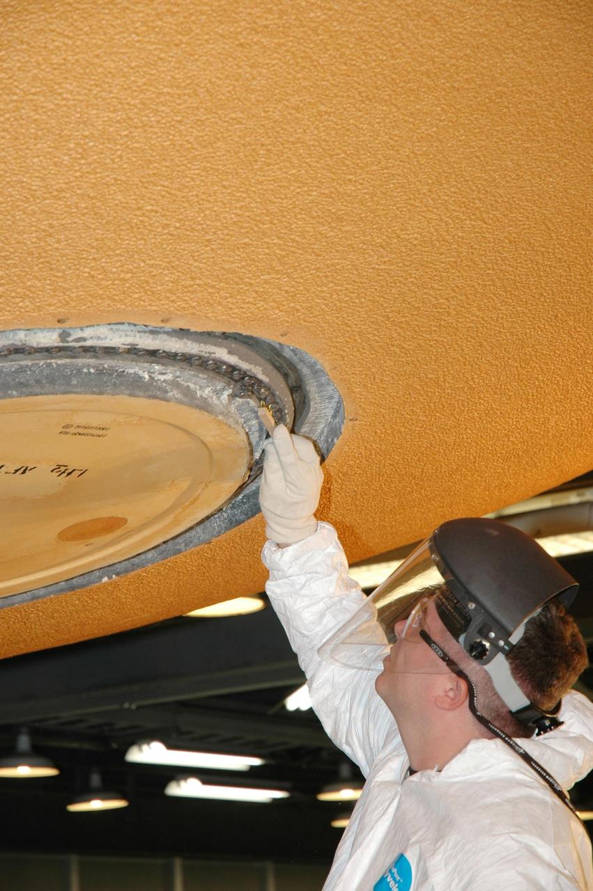 KENNEDY SPACE CENTER, FLA. - A Lockheed Martin technician from NASA's Michoud Assembly Facility in Louisiana cleans the area around the "manhole" on the external tank designated for mission STS-121. The work is part of the process in removing and replacing the external tank's four liquid hydrogen main engine cutoff sensors, which indicate whether the tank still has fuel during its climb to orbit. After the cleaning, the manhole will be removed to provide access to the area of the sensors for their removal. Photo credit: NASA/Jim Grossmann
