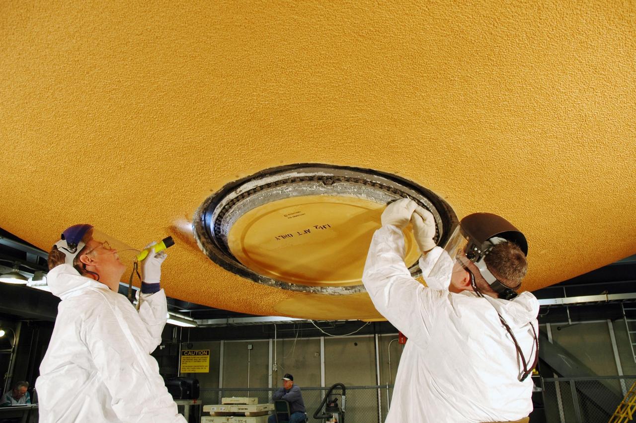 KENNEDY SPACE CENTER, FLA. - Lockheed Martin technicians from NASA's Michoud Assembly Facility in Louisiana inspect and clean the area around the "manhole" on the external tank designated for mission STS-121. The work is part of the process in removing and replacing the external tank's four liquid hydrogen main engine cutoff sensors, which indicate whether the tank still has fuel during its climb to orbit. After the cleaning, the manhole will be removed to provide access to the area of the sensors for their removal. Photo credit: NASA/Jim Grossmann
