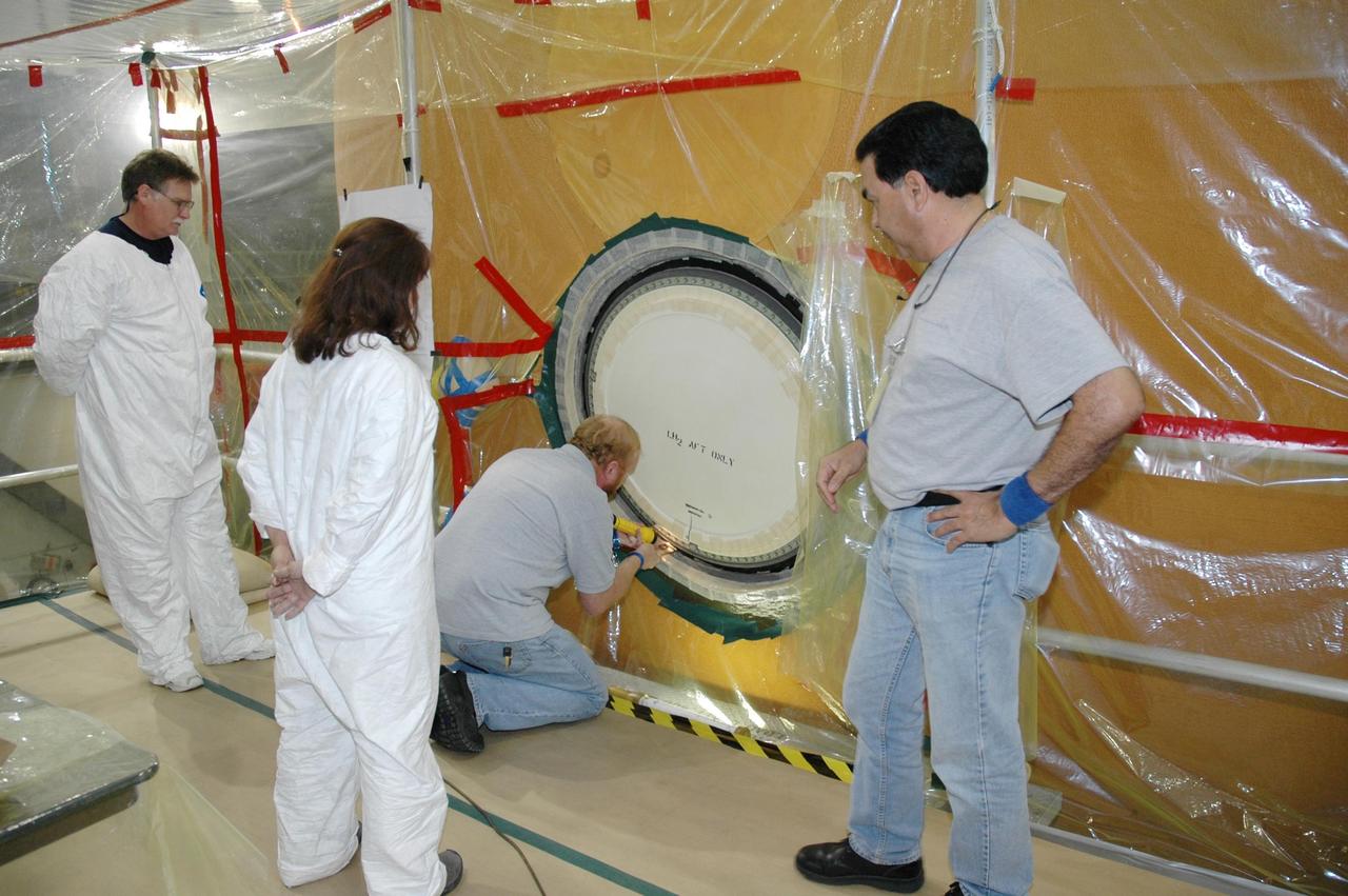 KENNEDY SPACE CENTER, FLA.  - In the transfer aisle of the Vehicle Assembly Building, workers prepare the cover, called the "manhole," on the bottom of external tank number 119 that will be refoamed.  The manhole was removed to access the area where the tank's four liquid hydrogen engine cutoff sensors were replaced.  The tank is being prepared to launch Space Shuttle Discovery on mission STS-121 in July.  Photo credit: NASA/Jim Grossmann