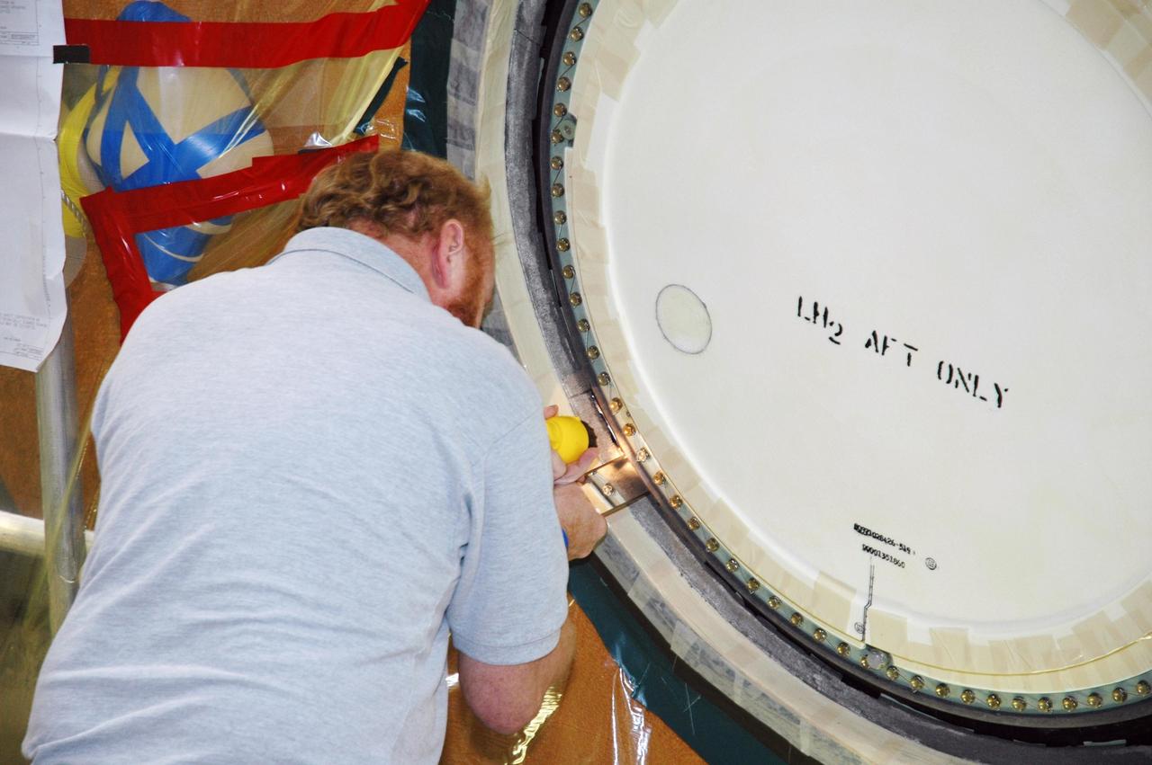 KENNEDY SPACE CENTER, FLA.  - In the transfer aisle of the Vehicle Assembly Building, a worker prepares the cover, called the "manhole," on the bottom of external tank number 119, for refoaming.  The manhole was removed to access the area where the tank's four liquid hydrogen engine cutoff sensors were replaced. The tank is being prepared to launch Space Shuttle Discovery on mission STS-121 in July.  Photo credit: NASA/Jim Grossmann