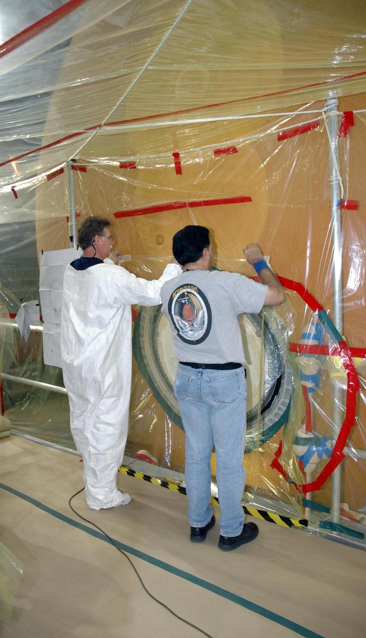 KENNEDY SPACE CENTER, FLA.  - In the transfer aisle of the Vehicle Assembly Building, workers prepare to refoam the cover, called the "manhole," on the bottom of external tank number 119. The manhole was removed to access the area where the tank's four liquid hydrogen engine cutoff sensors were replaced.  The tank is being prepared to launch Space Shuttle Discovery on mission STS-121 in July.  Photo credit: NASA/Jim Grossmann