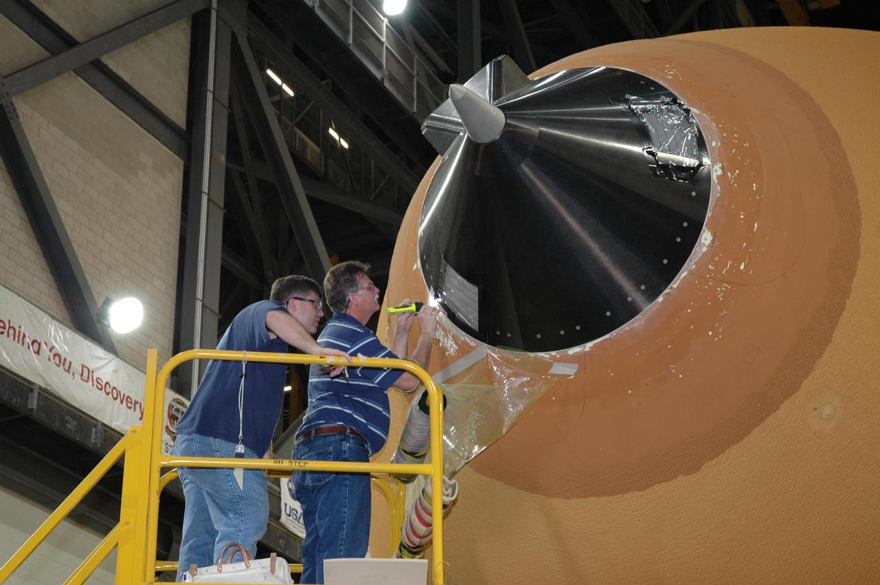 KENNEDY SPACE CENTER, FLA. - In the transfer aisle of the Vehicle Assembly Building, workers work on the rim around the nose cap of external tank number 119, the tank designated for mission STS-121. The cap was removed in order to install a new gaseous oxygen vent valve underneath. Vapors are created prior to launch as the liquid oxygen in the external tank boils off. At the forward end of each external tank propellant tank is a vent and relief valve that can be opened before launch for venting or by excessive tank pressure for relief. The vent function is available only before launch. Mission STS-121 to the International Space Station is scheduled for launch in July. Photo credit: NASA/Jim Grossmann