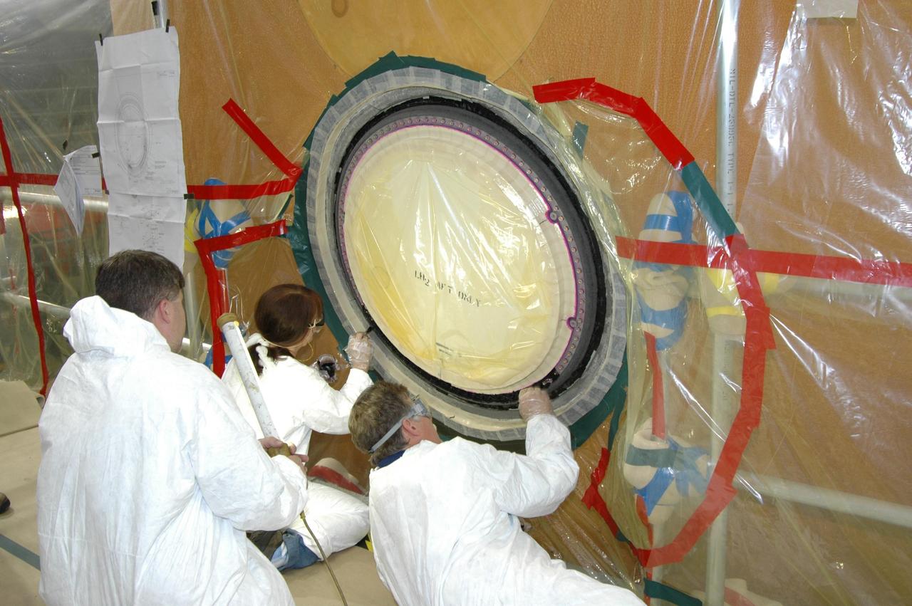 KENNEDY SPACE CENTER, FLA. -- In the transfer aisle of the Vehicle Assembly Building, workers pack type 2 ablator over the bolts around the "manhole" or cover on the bottom of external tank number 119. The manhole was removed to access the area where the tank's four liquid hydrogen engine cutoff sensors were replaced. The tank is being prepared to launch Space Shuttle Discovery on mission STS-121 in July. Photo credit: NASA/Jim Grossmann
