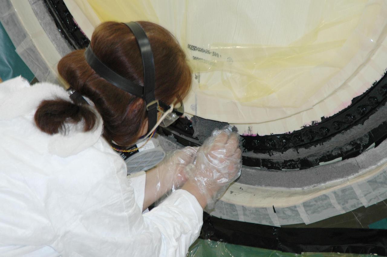 KENNEDY SPACE CENTER, FLA. -- In the transfer aisle of the Vehicle Assembly Building, a worker packs type 2 ablator over the bolts around the "manhole" or cover on the bottom of external tank number 119. The manhole was removed to access the area where the tank's four liquid hydrogen engine cutoff sensors were replaced. The tank is being prepared to launch Space Shuttle Discovery on mission STS-121 in July. Photo credit: NASA/Jim Grossmann