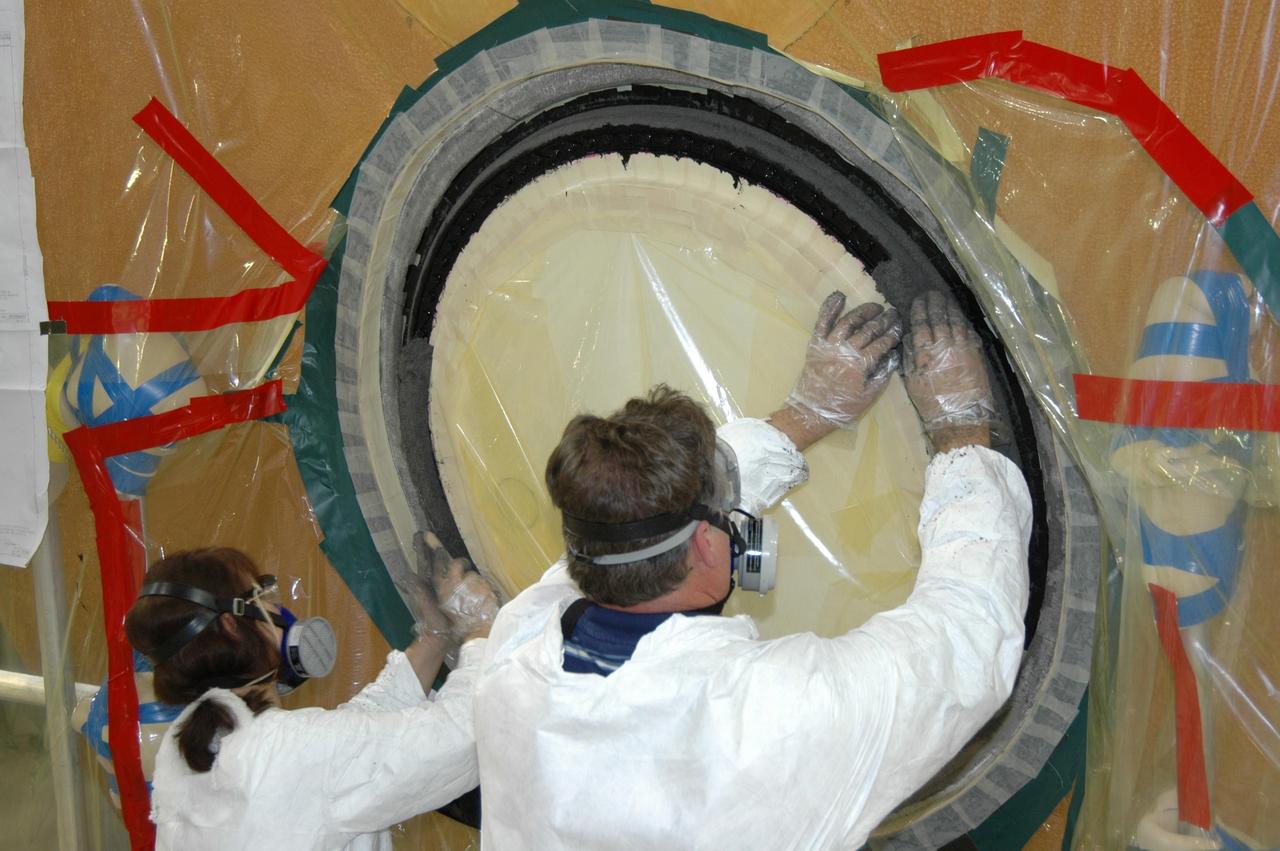 KENNEDY SPACE CENTER, FLA. -- In the transfer aisle of the Vehicle Assembly Building, workers pack type 2 ablator over the bolts around the "manhole" or cover on the bottom of external tank number 119. The manhole was removed to access the area where the tank's four liquid hydrogen engine cutoff sensors were replaced. The tank is being prepared to launch Space Shuttle Discovery on mission STS-121 in July. Photo credit: NASA/Jim Grossmann
