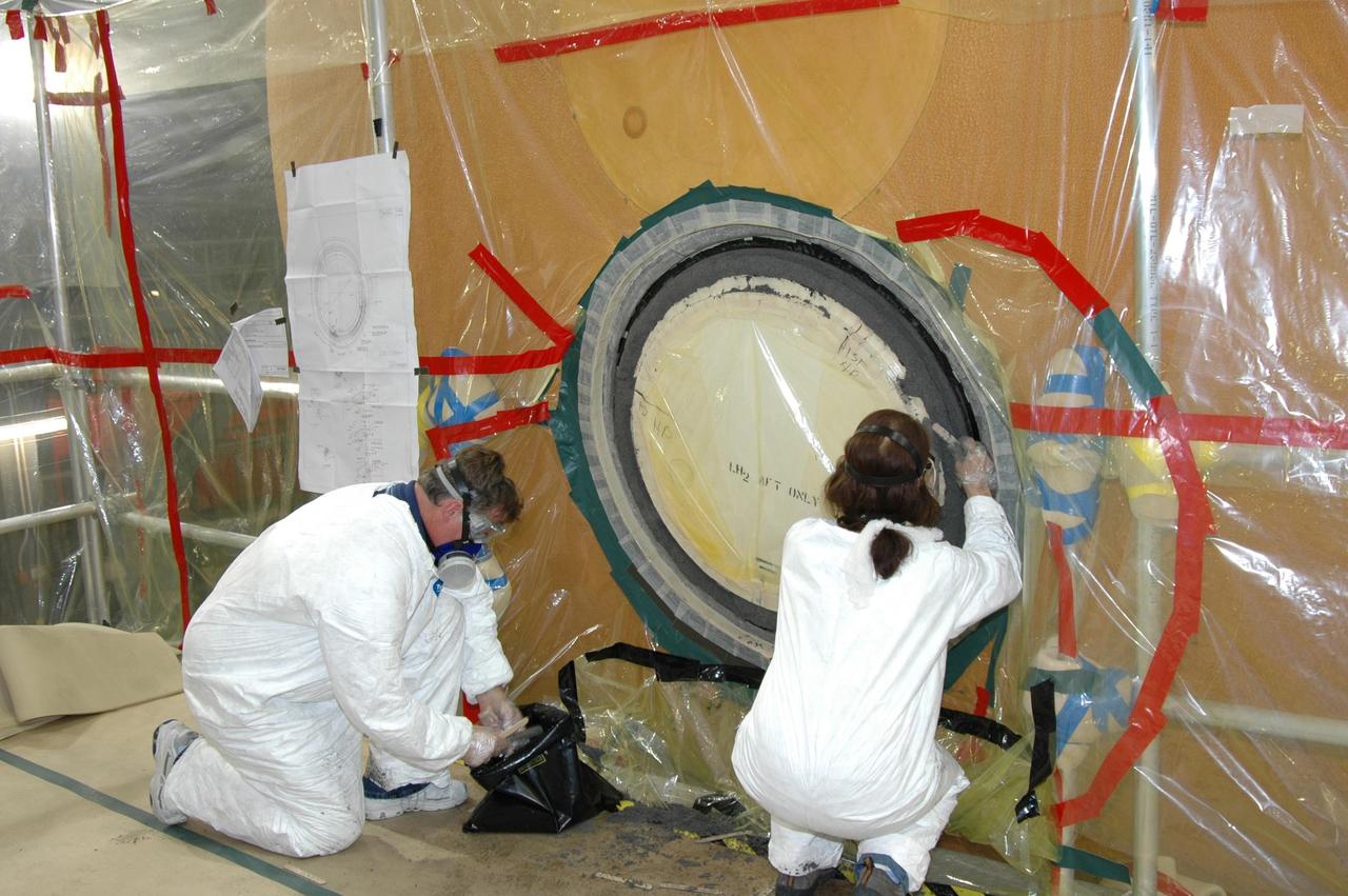 KENNEDY SPACE CENTER, FLA. -- In the transfer aisle of the Vehicle Assembly Building, workers pack type 2 ablator over the bolts around the "manhole" or cover on the bottom of external tank number 119. The manhole was removed to access the area where the tank's four liquid hydrogen engine cutoff sensors were replaced. The tank is being prepared to launch Space Shuttle Discovery on mission STS-121 in July. Photo credit: NASA/Jim Grossmann