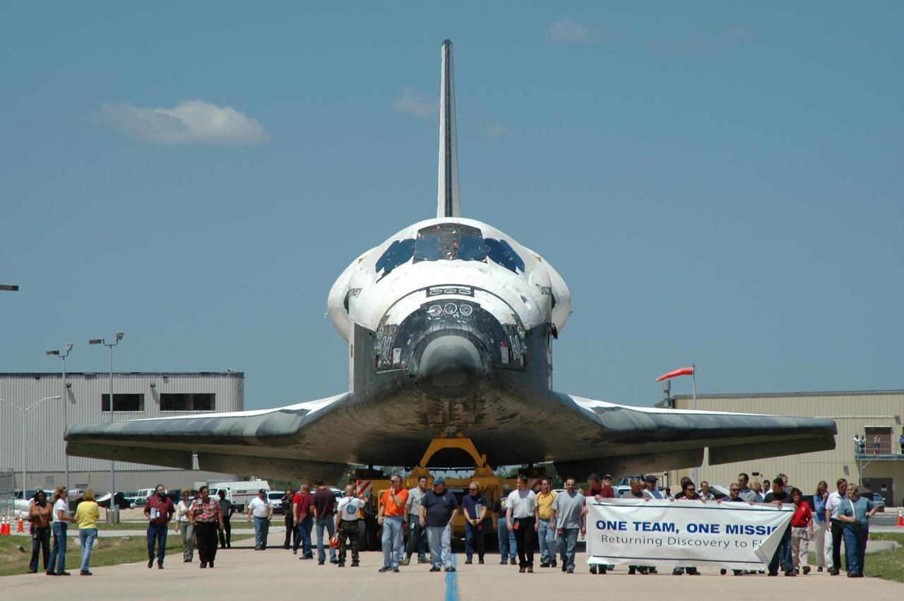 KENNEDY SPACE CENTER, FLA. - As the orbiter Discovery, sitting on an orbiter transporter, moves away from NASA's Orbiter Processing Facility toward the Vehicle Assembly Building (VAB), workers accompany the vehicle. The rollover to the VAB marks the start of the journey to the launch pad and, ultimately, launch. Once inside the VAB, Discovery will be raised to vertical and lifted up and over into high bay 3 for stacking with its redesigned external tank and twin solid rocket boosters. The rollout of Space Shuttle Discovery to Launch Pad 39B is expected in approximately a week. Launch of Discovery on mission STS-121 is scheduled to take place in a window extending July 1 to July 19. Photo credit: NASA/Jim Grossmann