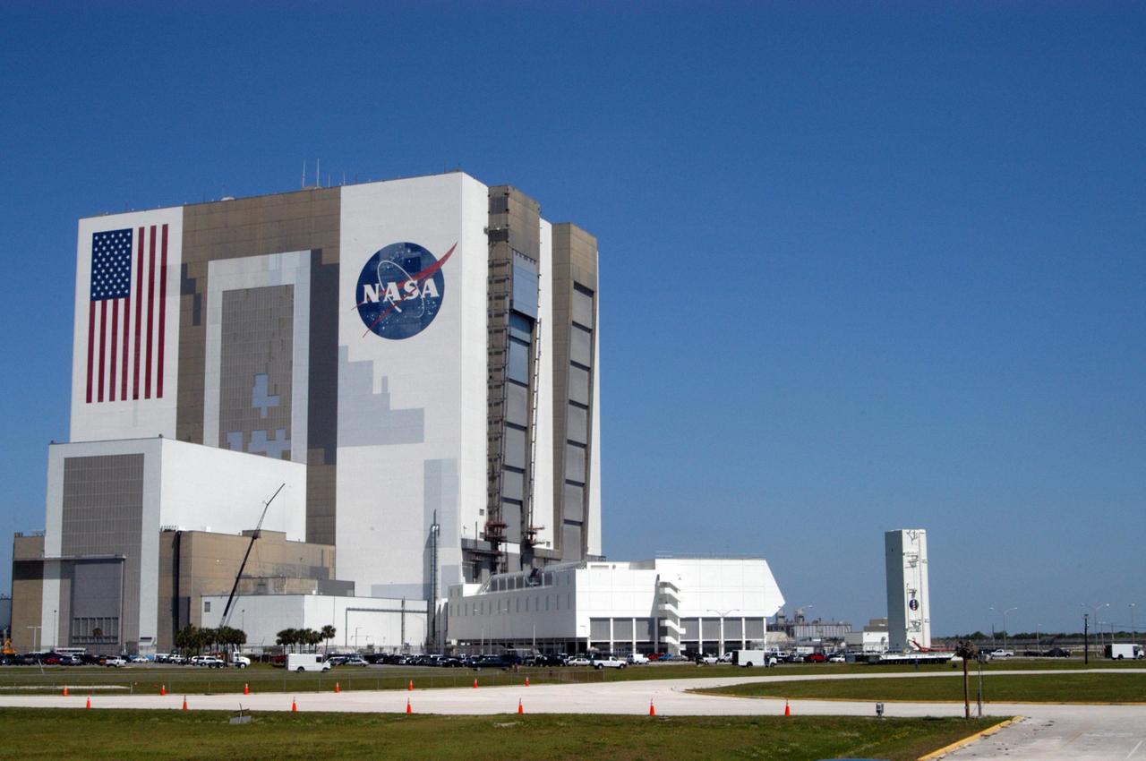 KENNEDY SPACE CENTER, FLA. -- The payload canister passes NASA's Vehicle Assembly Building and Launch Control Center on its way to Launch Pad 39B. Inside are the payloads for mission STS-121: the multi-purpose logistics module Leonardo, with supplies and equipment for the International Space Station; the lightweight multi-purpose experiment support structure carrier; and the integrated cargo carrier, with the mobile transporter reel assembly and a spare pump module. The payload will be transferred from the canister to Space Shuttle Discovery's payload bay at the pad. Discovery is scheduled to launch on mission STS-121 from Launch Pad 39B in a window that opens July 1 and extends to July 19. Photo credit: NASA/George Shelton