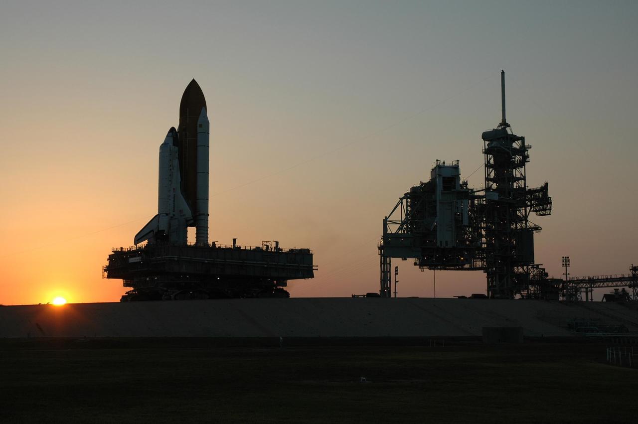 KENNEDY SPACE CENTER, FLA. --  The sun is setting as Space Shuttle Discovery nears its place on Launch Pad 39B at NASA's Kennedy Space Center. At right are the fixed and rotating service structures.  First motion was at 12:45 p.m. EDT. The shuttle rests on a mobile launcher platform and made the 4.2-mile journey from the Vehicle Assembly Building via the crawler-transporter beneath the platform.  The rollout is an important step before launch of Discovery on mission STS-121 to the International Space Station.  Discovery's launch is targeted for July 1 in a launch window that extends to July 19. During the 12-day mission, Discovery's crew will test new hardware and techniques to improve shuttle safety, as well as deliver supplies and make repairs to the station. Photo credit: NASA/Dimitri Gerondidakis