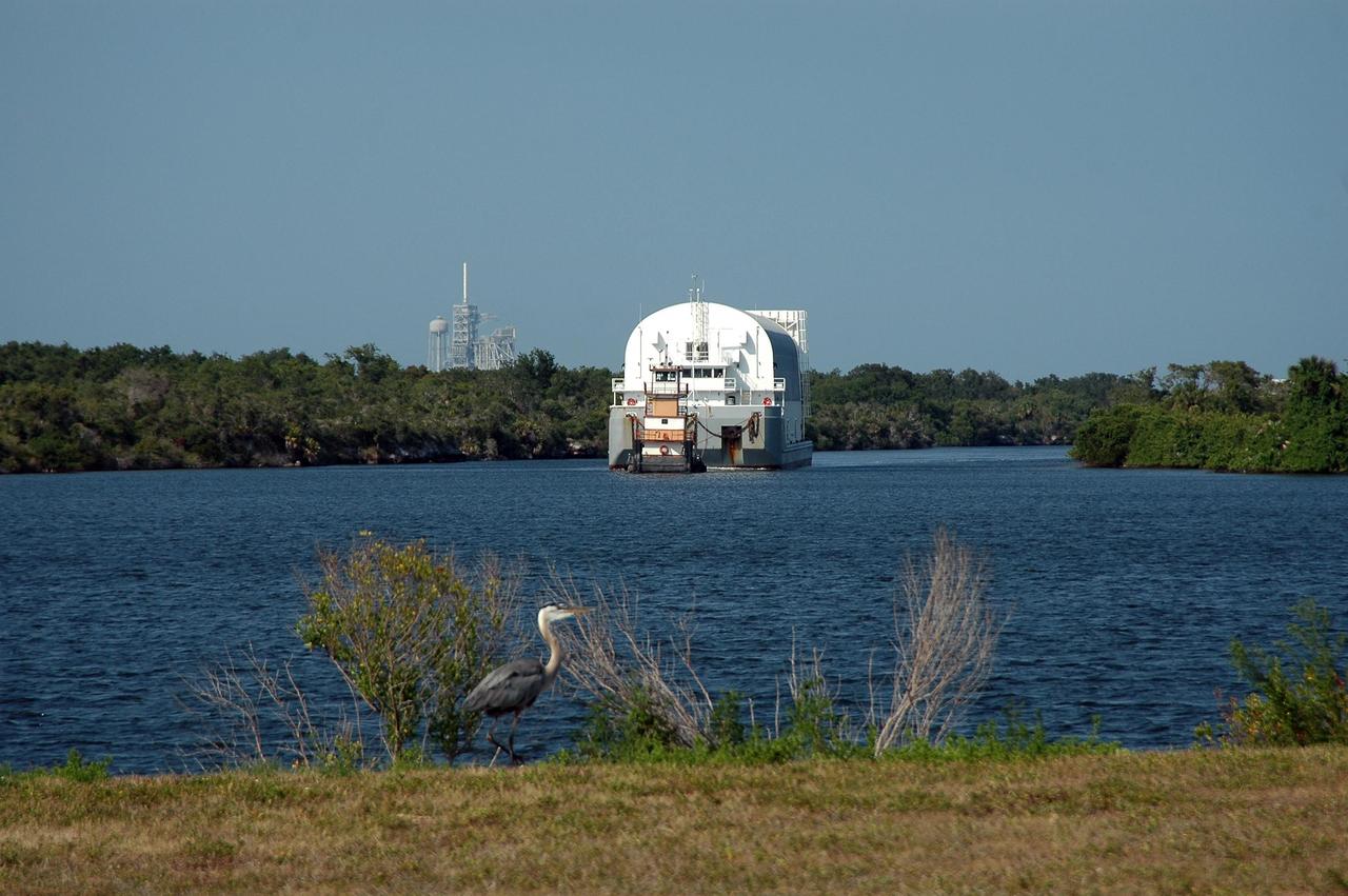 KENNEDY SPACE CENTER, FLA. -   A Great Blue Heron on the near bank has a front row perch for the arrival of the Pegasus barge being towed into the turn basin at the Launch Complex 39 Area.  The barge holds  the redesigned external fuel tank, designated ET-118, that will launch Space Shuttle Atlantis on the next shuttle mission, STS-115.  The tank was shipped from the Michoud Assembly Facility in New Orleans.  After off-loading, the tank will be moved into the Vehicle Assembly Building and lifted into a checkout cell for further work. The tank will fly with many major safety changes, including the removal of the protuberance air load ramps. Photo credit: NASA/Kim Shiflett