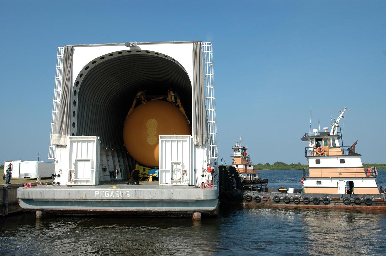 KENNEDY SPACE CENTER, FLA. -     Tug boats maneuver the Pegasus barge next to the dock in the turn basin at the Launch Complex 39 Area.  The barge holds the redesigned external fuel tank, seen inside, that will launch Space Shuttle Atlantis on the next shuttle mission, STS-115. The tank, designated ET-118, was shipped from the Michoud Assembly Facility in New Orleans.  After off-loading, the tank will be moved into the Vehicle Assembly Building and lifted into a checkout cell for further work. The tank will fly with many major safety changes, including the removal of the protuberance air load ramps. Photo credit: NASA/Kim Shiflett