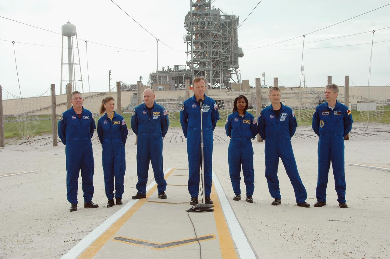 KENNEDY SPACE CENTER, FLA. - The STS-121 crew pause in their prelaunch activities to talk to the media.  They are standing in the landing area of the slidewire baskets.  At the microphone is Commander Steven Lindsey.  Behind him are (from left) Mission Specialists Michael Fossum and Lisa Nowak, Pilot Mark Kelly and Mission Specialists Stephanie Wilson, Piers Sellers and Thomas Reiter of Germany, who represents the European Space Agency.  The crew is at Kennedy for Terminal Countdown Demonstration Test activities. Over several days, the crew will practice emergency egress from the pad and suit up in their orange flight suits for the simulated countdown to launch. Space Shuttle Discovery is designated to launch July 1 on mission STS-121.  It will carry supplies to the International Space Station.  Photo credit: NASA/Kim Shiflett