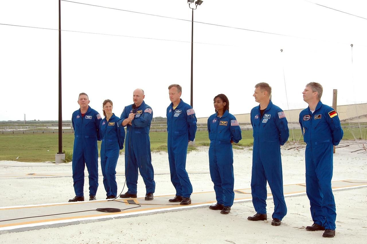 KENNEDY SPACE CENTER, FLA. - The STS-121 crew pause in their prelaunch activities to talk to the media.  They are standing in the landing area of the slidewire baskets. With the microphone is Pilot Mark Kelly.  The crew members are (from left) Mission Specialists Michael Fossum and Lisa Nowak, Kelly, Commander Steven Lindsey, and Mission Specialists Stephanie Wilson, Piers Sellers and Thomas Reiter of Germany, who represents the European Space Agency.  The crew is at Kennedy for Terminal Countdown Demonstration Test activities. Over several days, the crew will practice emergency egress from the pad and suit up in their orange flight suits for the simulated countdown to launch. Space Shuttle Discovery is designated to launch July 1 on mission STS-121.  It will carry supplies to the International Space Station.  Photo credit: NASA/Kim Shiflett
