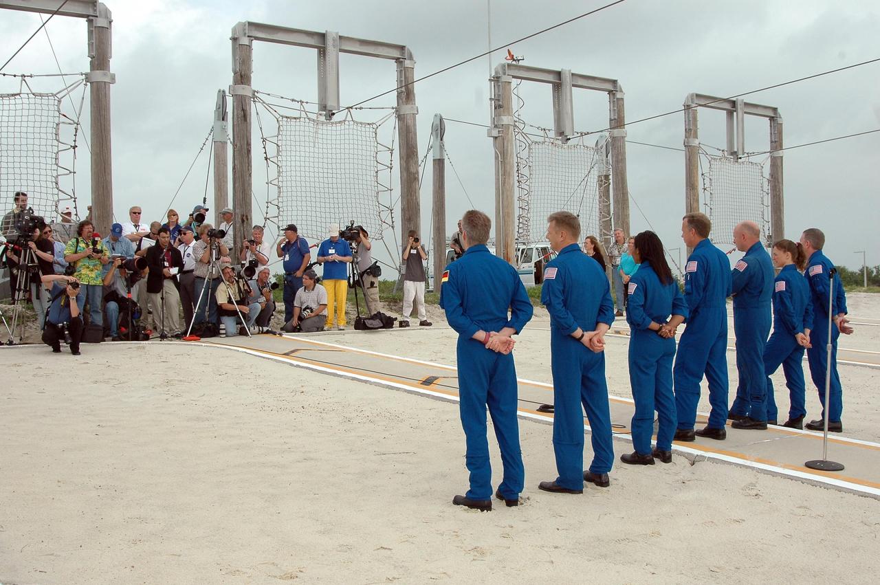 KENNEDY SPACE CENTER, FLA. - The STS-121 crew pause in their prelaunch activities to talk to the media, gathered at left.  They are standing in the landing area of the slidewire baskets. The crew members facing them are (from left)  Mission Specialists Thomas Reiter of Germany, who represents the European Space Agency, Piers Sellers, Stephanie Wilson, Commander Steven Lindsey, Pilot Mark Kelly, and Mission Specialists Lisa Nowak and Michael Fossum.  The crew is at Kennedy for Terminal Countdown Demonstration Test activities. Over several days, the crew will practice emergency egress from the pad and suit up in their orange flight suits for the simulated countdown to launch. Space Shuttle Discovery is designated to launch July 1 on mission STS-121.  It will carry supplies to the International Space Station.  Photo credit: NASA/Kim Shiflett