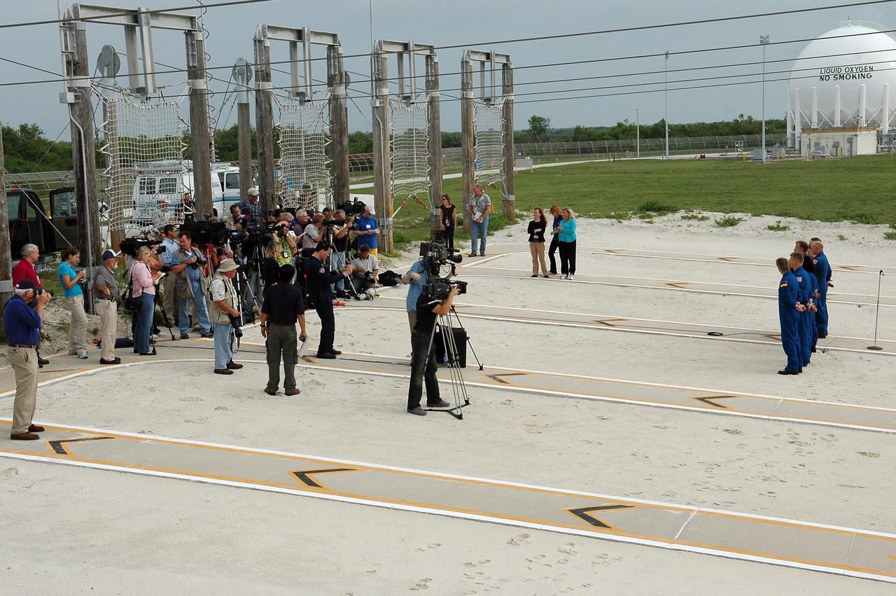 KENNEDY SPACE CENTER, FLA. - The STS-121 crew pause in their prelaunch activities to talk to the media, gathered at left. They are standing in the landing area of the slidewire baskets. The crew members facing them are (from left) Mission Specialists Thomas Reiter of Germany, who represents the European Space Agency, Piers Sellers, Stephanie Wilson, Commander Steven Lindsey, Pilot Mark Kelly, and Mission Specialists Lisa Nowak and Michael Fossum. The crew is at Kennedy for Terminal Countdown Demonstration Test activities. Over several days, the crew will practice emergency egress from the pad and suit up in their orange flight suits for the simulated countdown to launch. Space Shuttle Discovery is designated to launch July 1 on mission STS-121. It will carry supplies to the International Space Station. Photo credit: NASA/Kim Shiflett