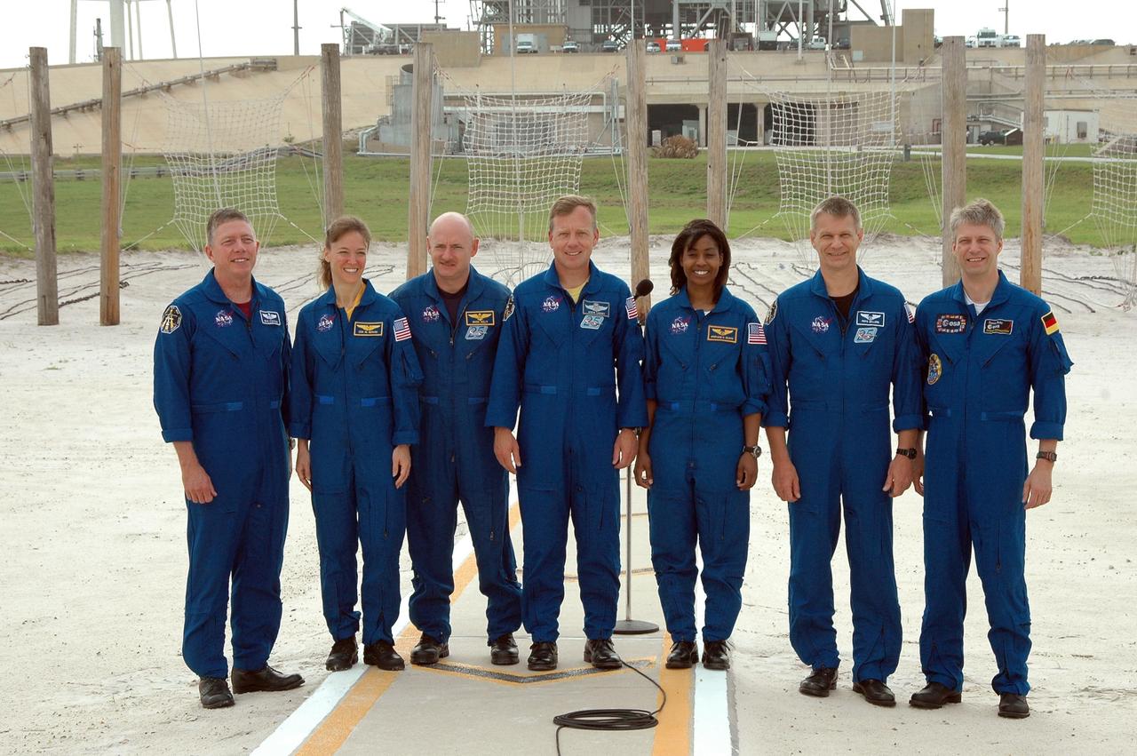 KENNEDY SPACE CENTER, FLA. - The STS-121 crew pose for the media, concluding a press conference held in the landing area of the slidewire baskets. The crew members facing them are (from left) The crew members are (from left) Mission Specialists Michael Fossum and Lisa Nowak, Pilot Mark Kelly, Commander Steven Lindsey, and Mission Specialists Stephanie Wilson, Piers Sellers and Thomas Reiter of Germany, who represents the European Space Agency. The crew is at Kennedy for Terminal Countdown Demonstration Test activities. Over several days, the crew will practice emergency egress from the pad and suit up in their orange flight suits for the simulated countdown to launch. Space Shuttle Discovery is designated to launch July 1 on mission STS-121. It will carry supplies to the International Space Station. Photo credit: NASA/Kim Shiflett