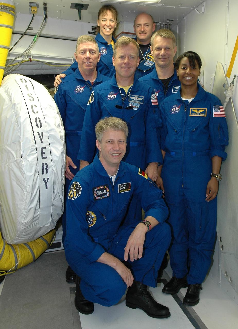 KENNEDY SPACE CENTER, FLA. - The STS-121 crew pose outside of Space Shuttle Discovery's hatch during prelaunch training at Launch Pad 39B. Kneeling in front is Mission Specialist Thomas Reiter of Germany, who represents the European Space Agency. Standing behind are (from left) Mission Specialists Thomas Fossum and Lisa Nowak, Commander Steven Lindsey (center), Pilot Mark Kelly, and Mission Specialists Piers Sellers and Stephanie Wilson. The crew is at Kennedy for Terminal Countdown Demonstration Test activities, including emergency egress training from the pad. They will also suit up in their orange flight suits for a simulated countdown to launch. Discovery is designated to launch July 1 on mission STS-121. It will carry supplies to the International Space Station. Photo credit: NASA/Kim Shiflett