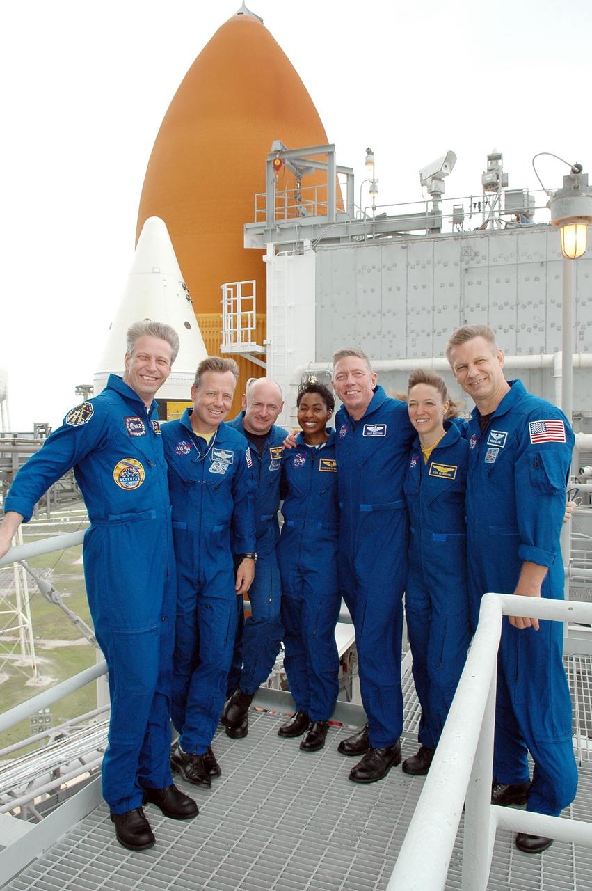 KENNEDY SPACE CENTER, FLA. - During emergency egress training at the pad, the STS-121 crew poses for a photo on the upper level. From left are Mission Specialist Thomas Reiter, Commander Steven Lindsey, Pilot Mark Kelly, and Mission Specialists Stephanie Wilson, Michael Fossum, Lisa Nowak and Piers Sellers. Behind them can be seen the top of a solid rocket booster and the external tank, part of the configuration for Space Shuttle Discovery. The crew is at Kennedy for Terminal Countdown Demonstration Test activities, including emergency egress training from the pad. They will also suit up in their orange flight suits for a simulated countdown to launch. Discovery is designated to launch July 1 on mission STS-121. It will carry supplies to the International Space Station. Photo credit: NASA/Kim Shiflett