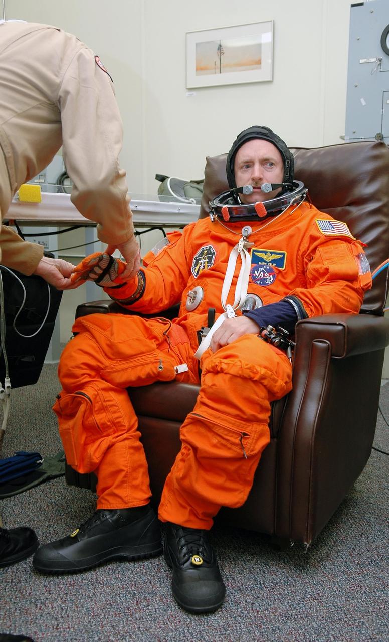 KENNEDY SPACE CENTER, FLA. - STS-121 Pilot Mark Kelly is helped with his glove after donning his launch and entry suit in preparation for the simulated countdown he and other crew members will undertake. The crew is taking part in Terminal Countdown Demonstration Test activities, including the dress rehearsal for launch. Mission STS-121 is scheduled to be launched July 1.  Photo credit: NASA/Kim Shiflett