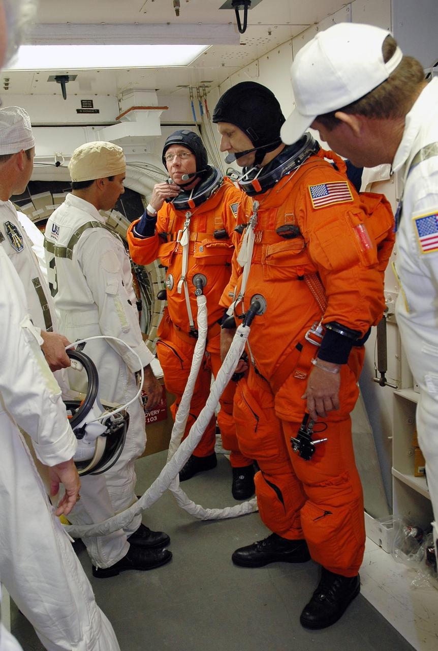 KENNEDY SPACE CENTER, FLA. -  In the White Room on Launch Pad 39B, STS-121 Mission Specialists Michael Fossum (center) and Piers Sellers have their launch suits checked by the closeout crew before entering Space Shuttle Discovery. They are connected to portable cooling units keeping them cool while waiting to enter Space Shuttle Discovery. The crew is taking part in a full dress rehearsal for launch, including countdown and culminating in main engine cutoff. The rehearsal is the final part of Terminal Countdown Demonstration Test (TCDT) activities that the crew has been involved in for two days. TCDT provides the crew of each mission an opportunity to participate in various simulated countdown activities, including equipment familiarization and emergency egress training. Mission STS-121 is scheduled to be launched July 1. Photo credit: NASA/Amanda Diller