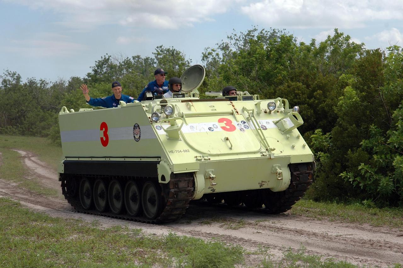 KENNEDY SPACE CENTER, FLA. -   Under the watchful eye of Capt. George Hoggard (left front), who is astronaut rescue team leader, STS-121 Commander Steven Lindsey takes his turn driving an M-113, which is an armored personnel carrier.  Behind Lindsey and Hoggard are Mission Specialists Piers Sellers (waving) and Michael Fossum.  The STS-121 crew is taking turns driving the M-113 as part of Terminal Countdown Demonstration Test activities, which include emergency egress training from the pad and a simulated countdown.   Mission STS-121 is designated for launch on July 1.   Photo credit: NASA/Kim Shiflett