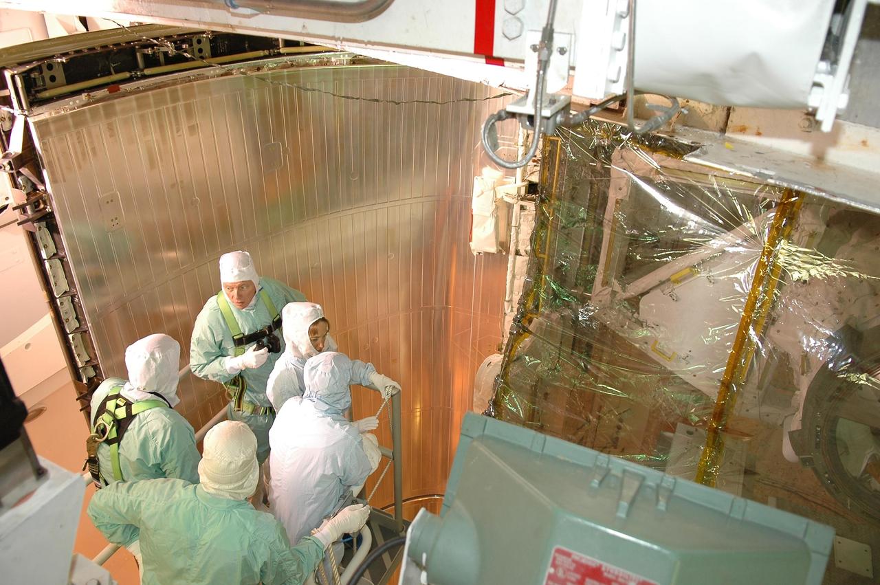 KENNEDY SPACE CENTER, FLA. - Inside the payload changeout room on Launch Pad 39B, STS-121 Mission Specialists Michael Fossum and Lisa Nowak (facing the camera) get a look at part of the payload for the mission. They are dressed in clean room suits, appropriate for the environmentally clean or "white room" condition in which the payload resides before being transferred to the shuttle's payload bay. The payload includes the multi-purpose logistics module Leonardo, with supplies and equipment for the International Space Station; the lightweight multi-purpose experiment support structure carrier; and the integrated cargo carrier. Crew members are at NASA's Kennedy Space Center for Terminal Countdown Demonstration Test activities, which include equipment familiarization and a simulated launch countdown. Mission STS-121 is scheduled for launch on Space Shuttle Discovery on July 1. Photo credit: NASA/Kim Shiflett