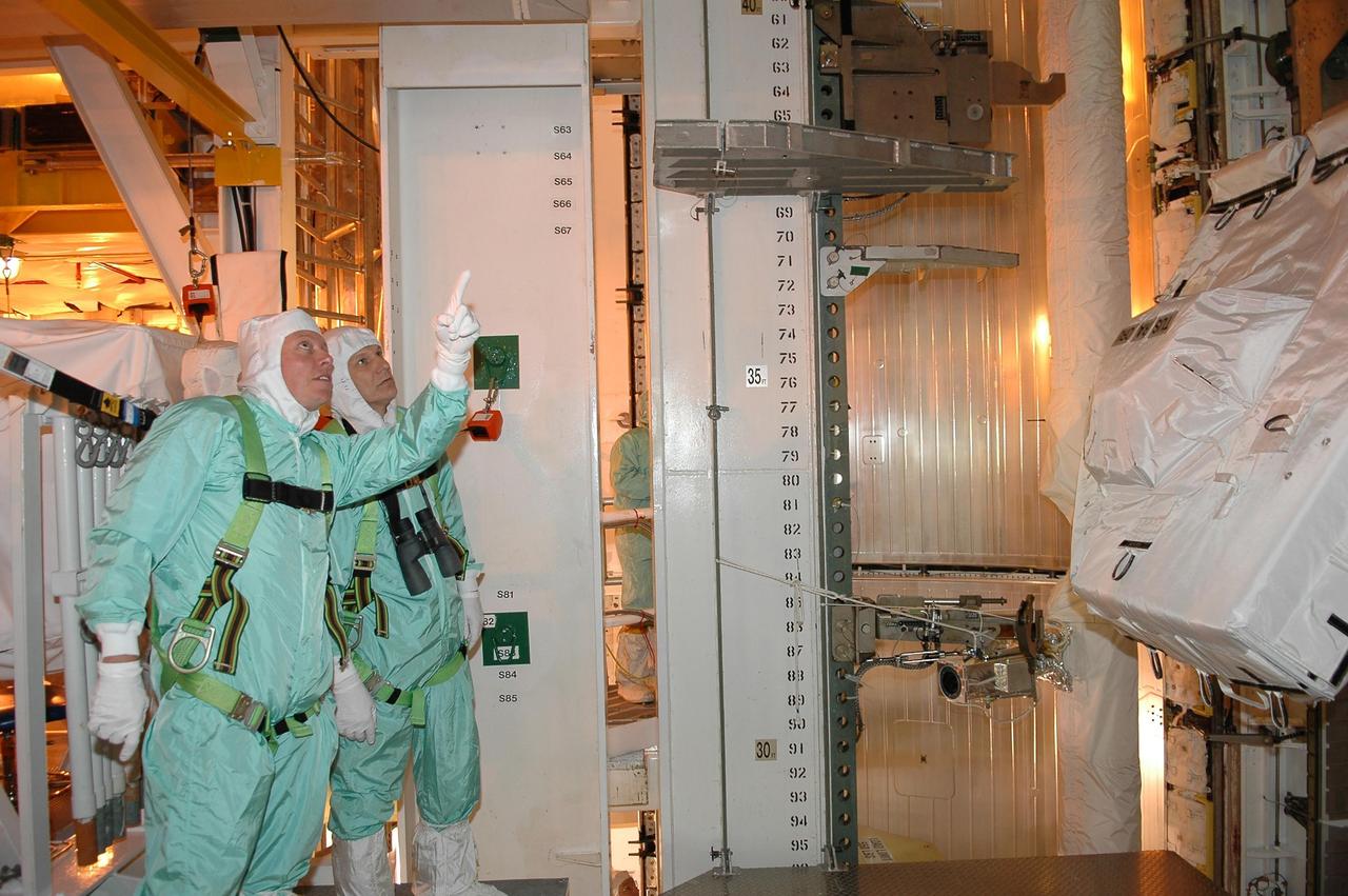 KENNEDY SPACE CENTER, FLA. - Inside the payload changeout room on Launch Pad 39B, STS-121 Mission Specialists Michael Fossum (left) and Piers Sellers check out part of the payload for the mission. They are dressed in clean room suits, appropriate for the environmentally clean or "white room" condition in which the payload resides before being transferred to the shuttle's payload bay. The payload includes the multi-purpose logistics module Leonardo, with supplies and equipment for the International Space Station; the lightweight multi-purpose experiment support structure carrier; and the integrated cargo carrier. Crew members are at NASA's Kennedy Space Center for Terminal Countdown Demonstration Test activities, which include equipment familiarization and a simulated launch countdown. Mission STS-121 is scheduled for launch on Space Shuttle Discovery on July 1. Photo credit: NASA/Kim Shiflett